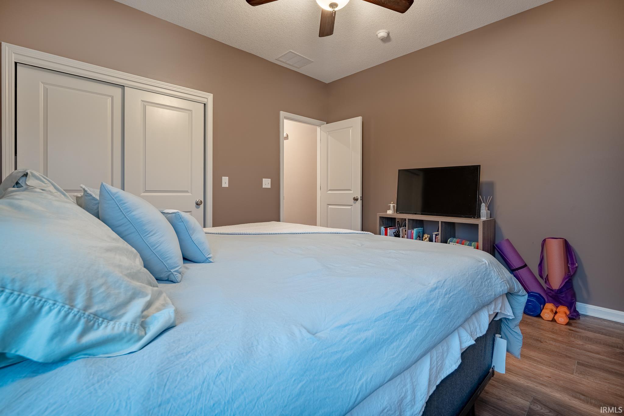 Bedroom featuring wood finished floors, a closet, a textured ceiling, and a ceiling fan