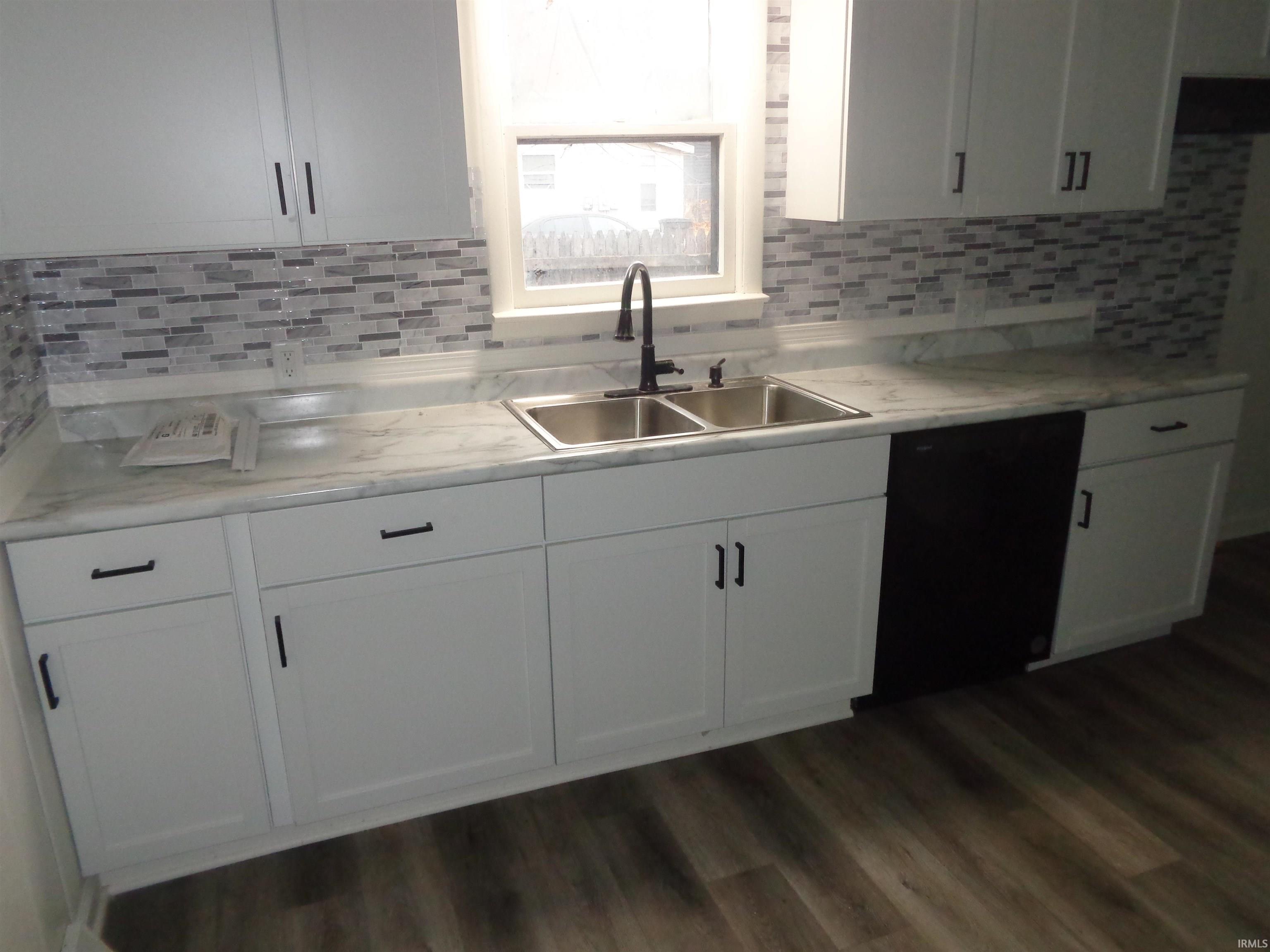 Kitchen featuring light countertops, black dishwasher, white cabinetry, and dark wood-type flooring