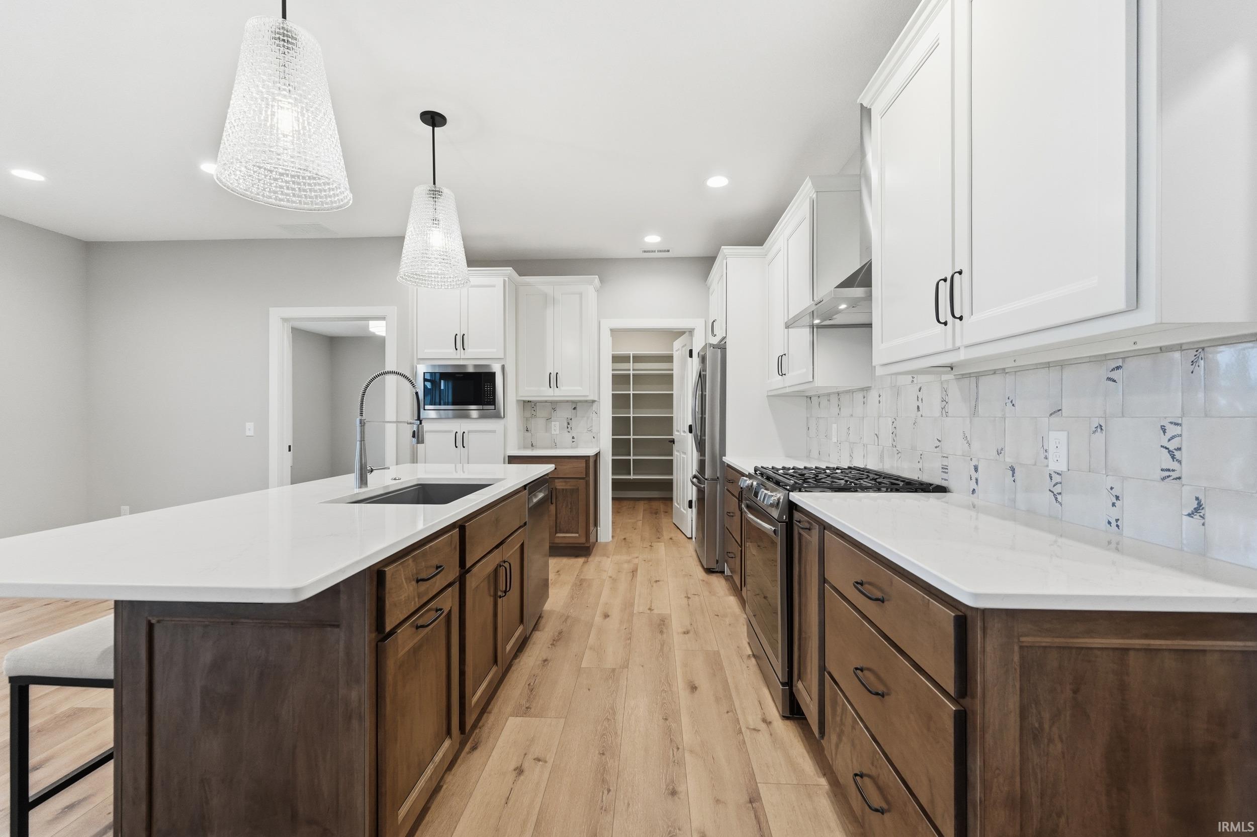 Kitchen featuring white cabinets, light wood-style flooring, a center island with sink, stainless steel appliances, and dark brown cabinetry