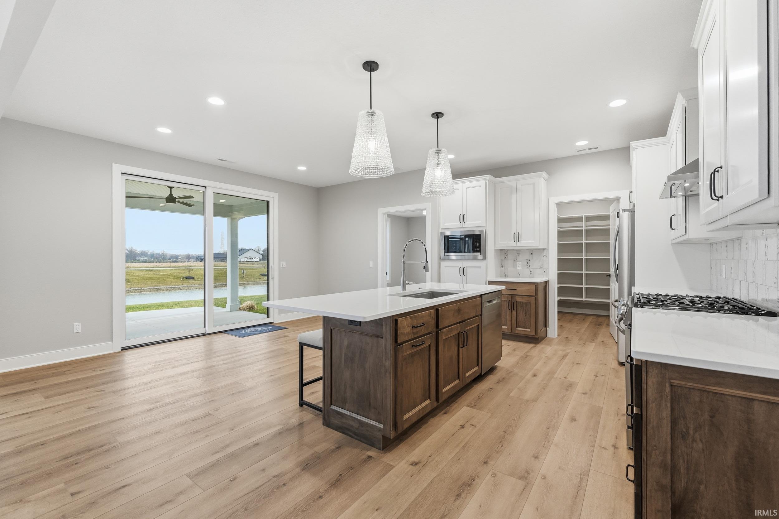 Kitchen with backsplash, a kitchen breakfast bar, dark brown cabinetry, light wood finished floors, and an island with sink