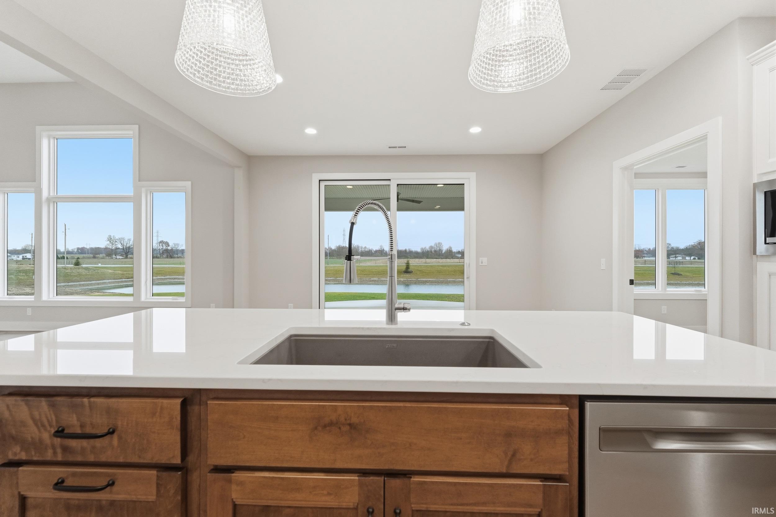 Kitchen featuring stainless steel dishwasher, brown cabinets, recessed lighting, a water view, and light stone counters