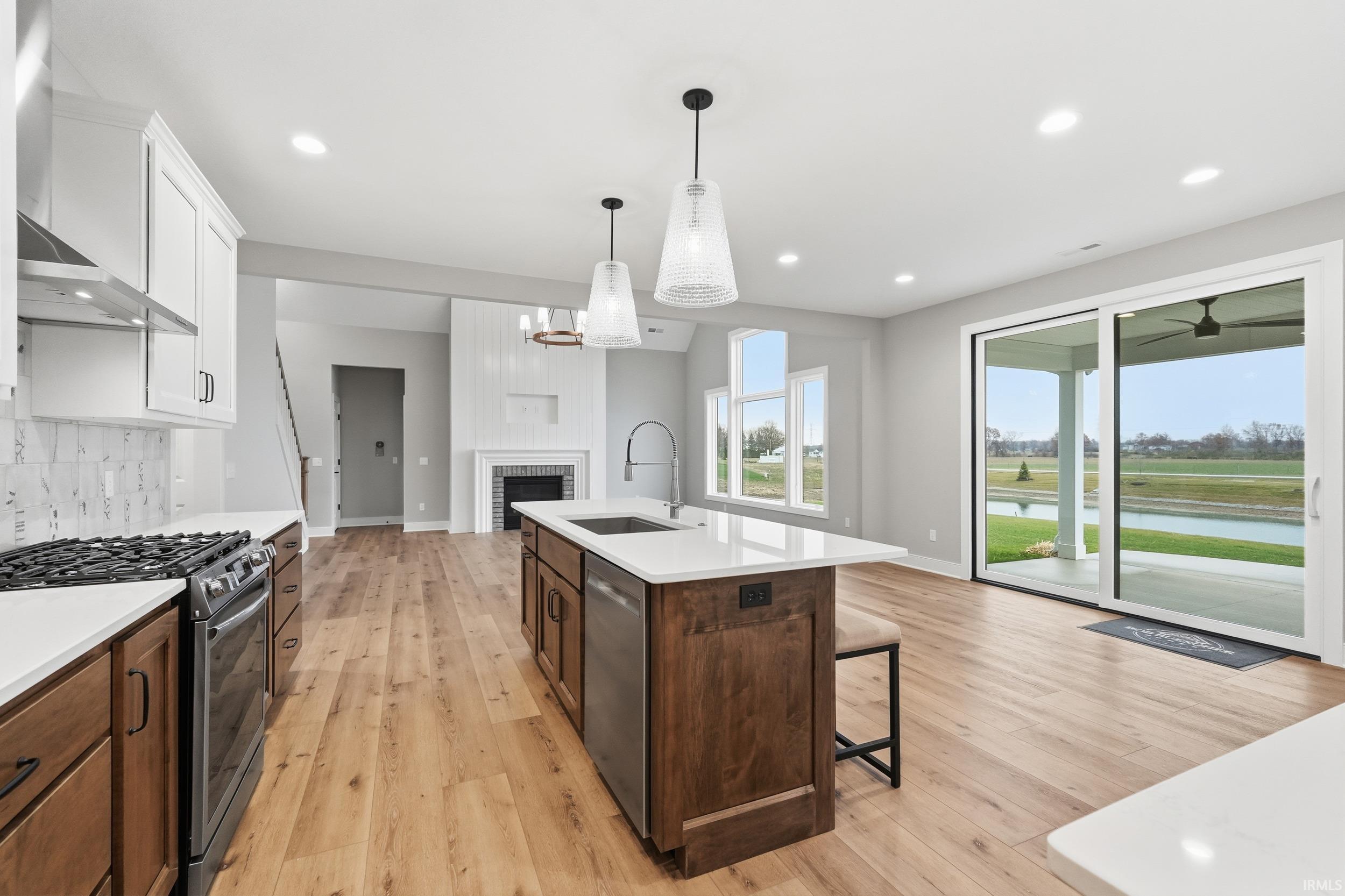 Kitchen featuring stainless steel appliances, wall chimney exhaust hood, backsplash, pendant lighting, and a brick fireplace