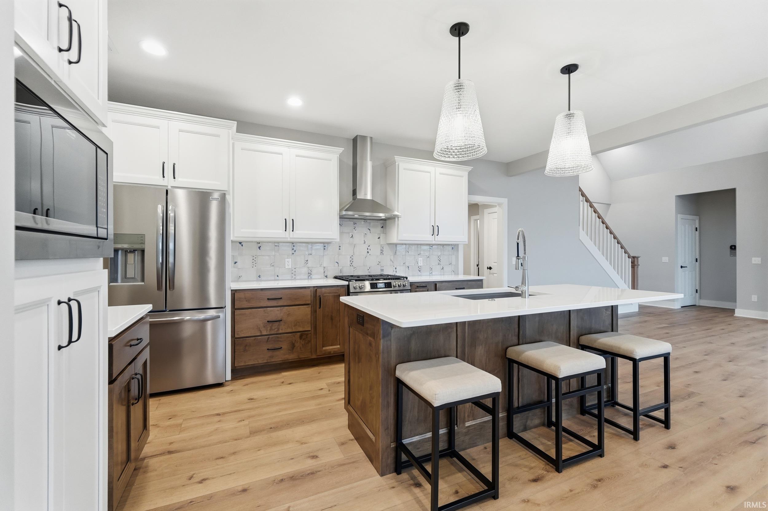 Kitchen with white cabinets, appliances with stainless steel finishes, a breakfast bar, an island with sink, and light wood-style floors