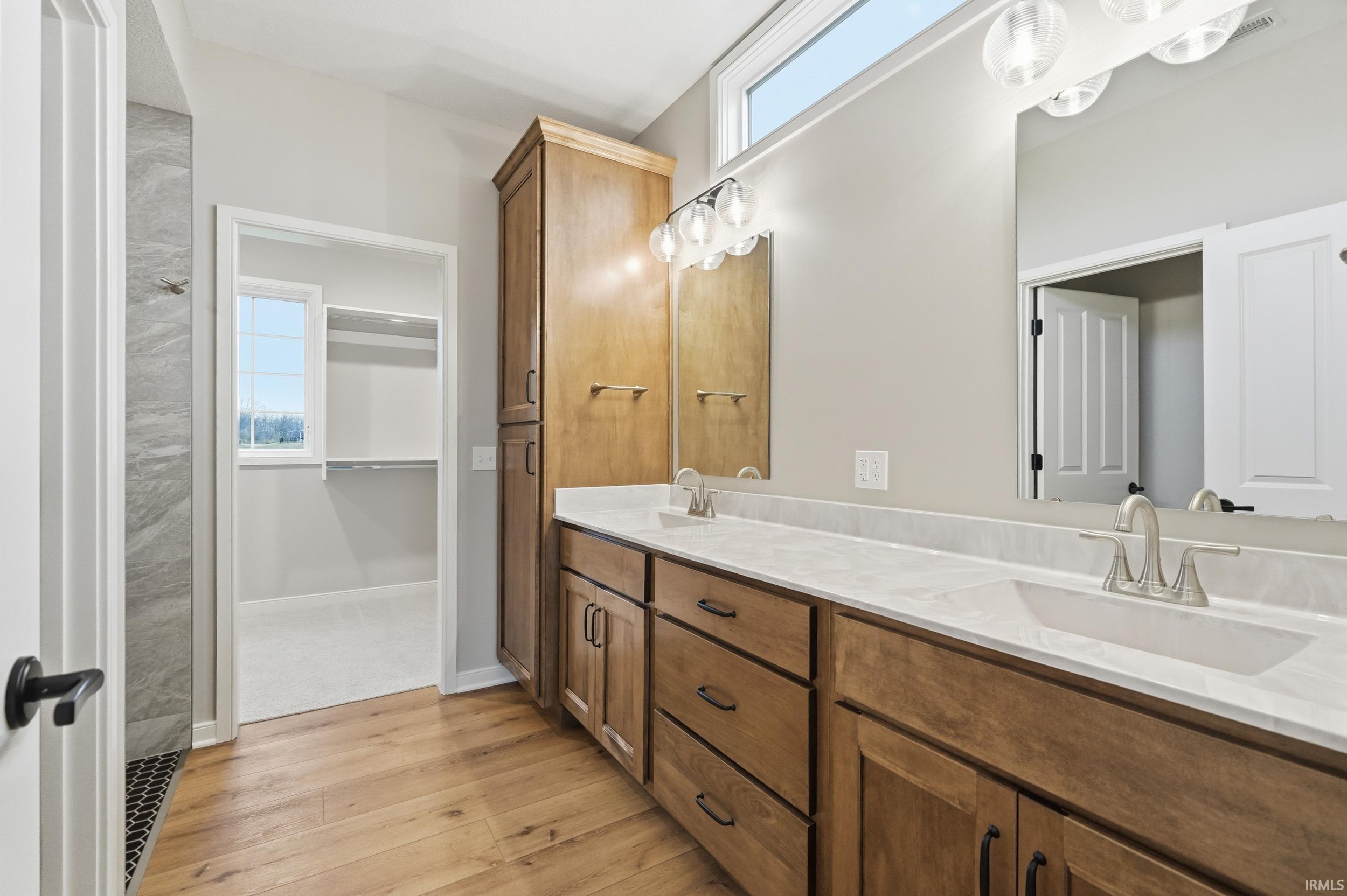 Full bathroom featuring light wood finished floors, double vanity, and a spacious closet