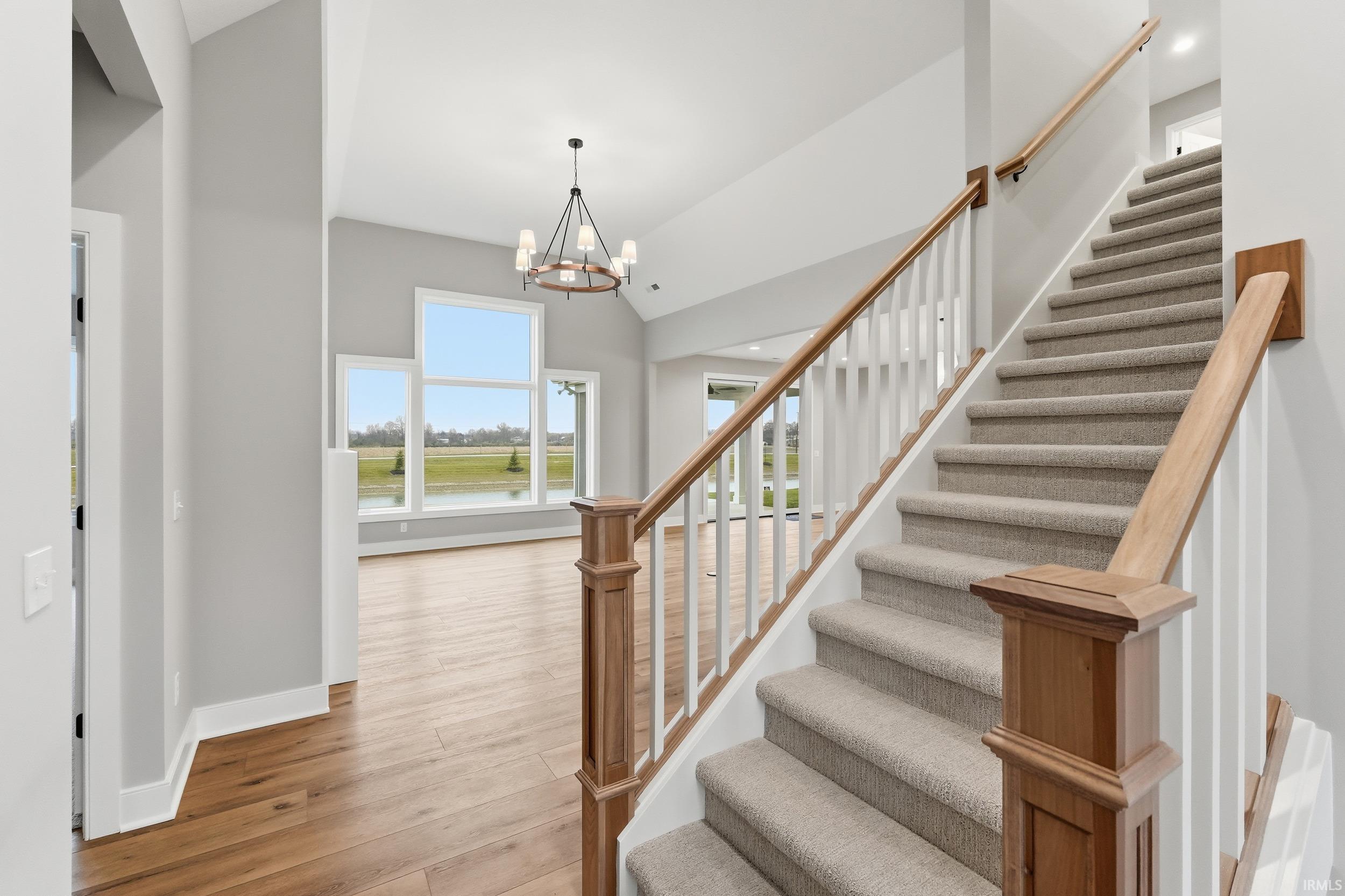 Stairs featuring wood finished floors, a chandelier, and high vaulted ceiling