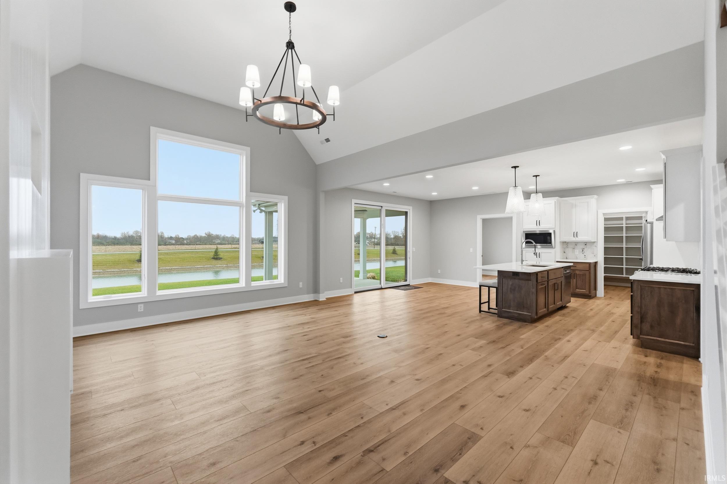 Unfurnished living room featuring a chandelier, light wood-type flooring, and lofted ceiling