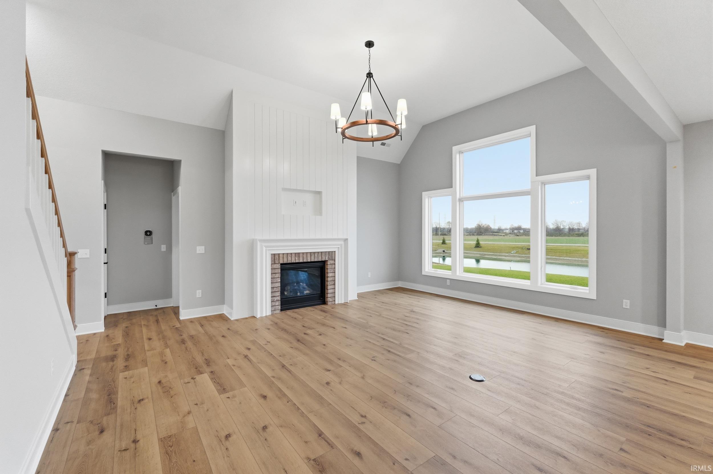Unfurnished living room featuring vaulted ceiling, stairway, light wood-style flooring, a fireplace, and a chandelier