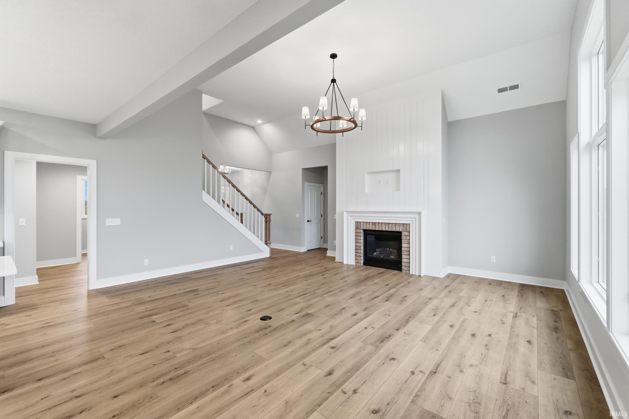 Unfurnished living room featuring vaulted ceiling, light wood-style flooring, a chandelier, stairway, and a fireplace