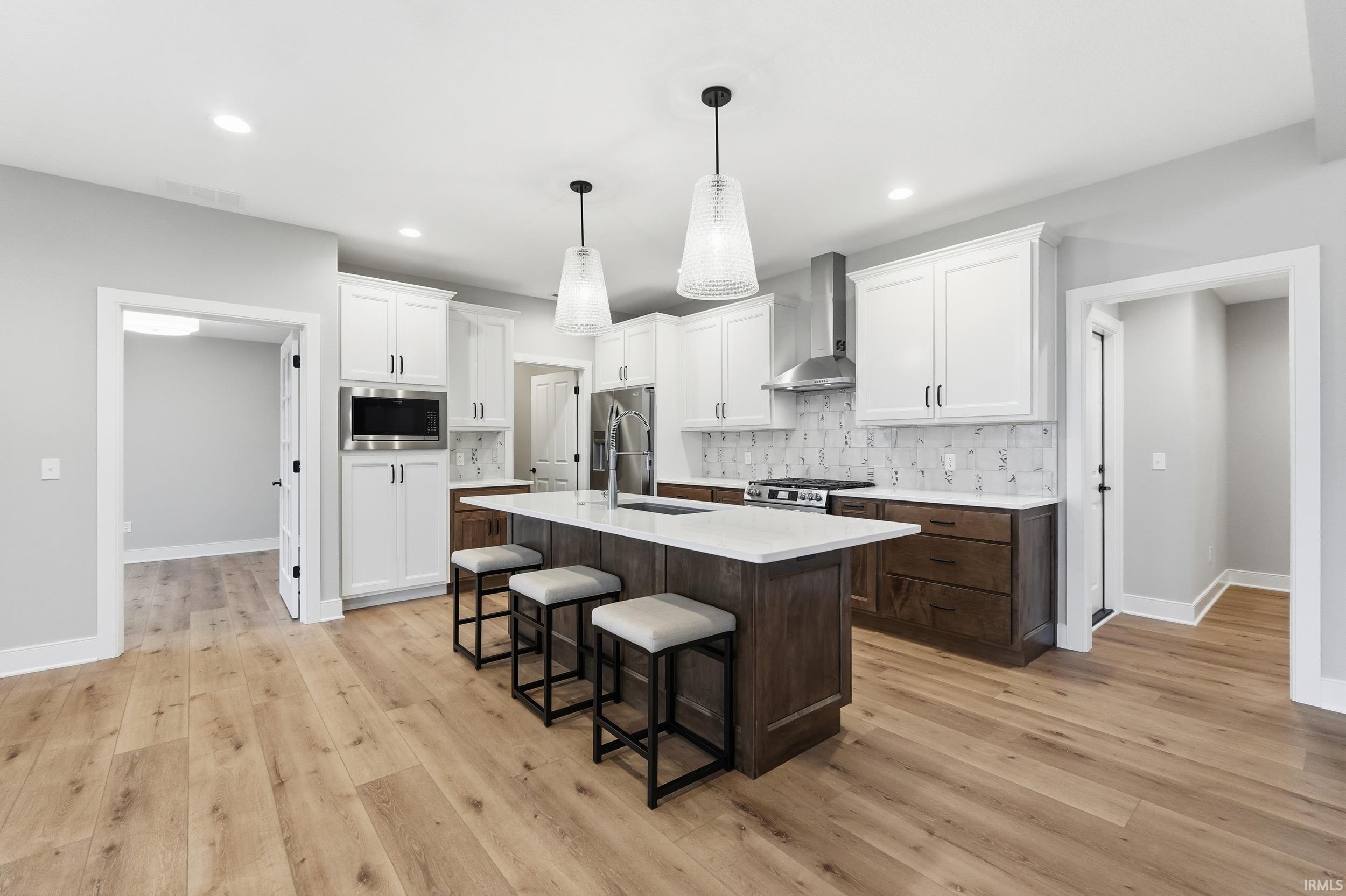 Kitchen with dark brown cabinets, white cabinetry, a kitchen breakfast bar, decorative light fixtures, and an island with sink