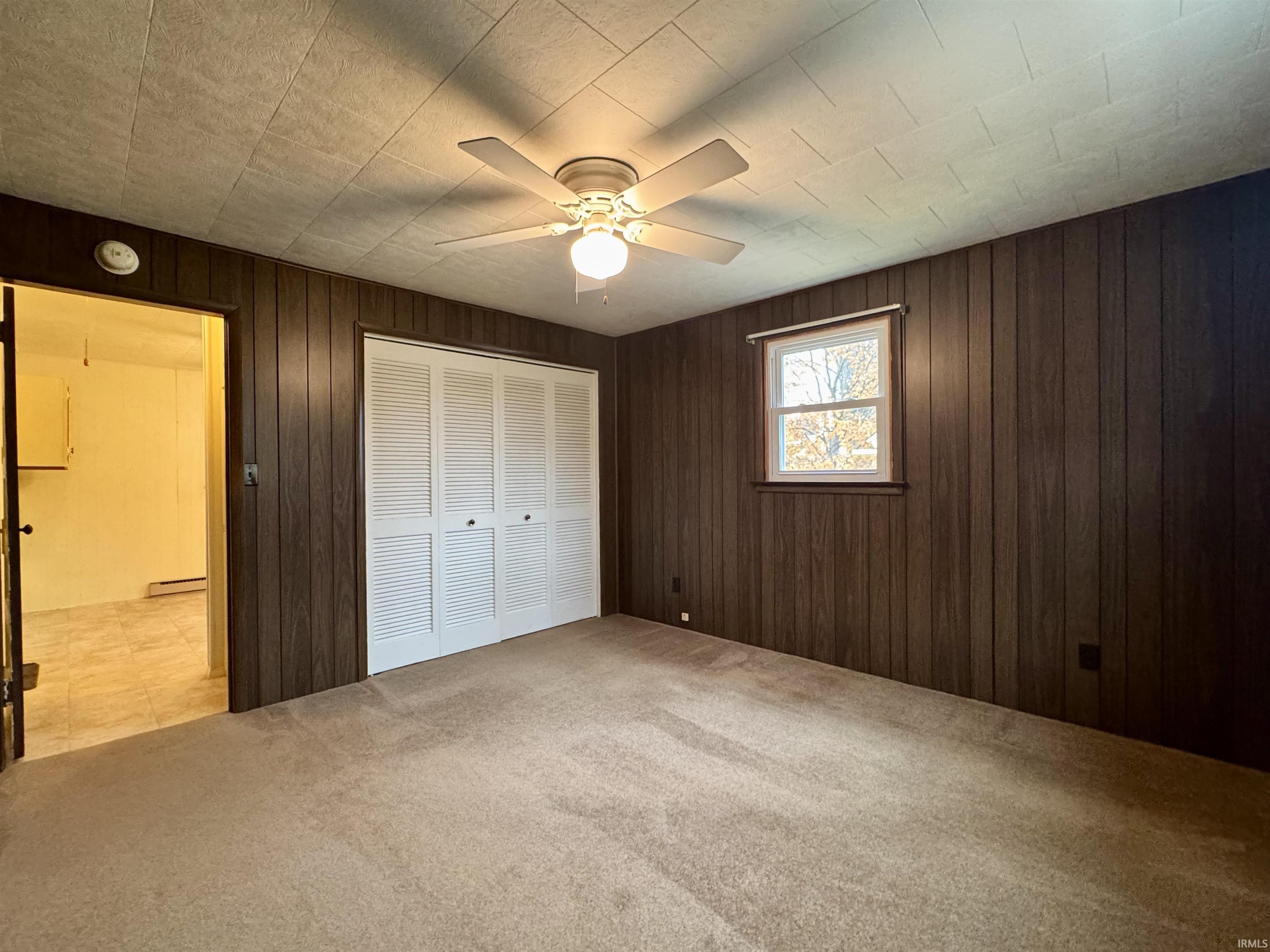 Unfurnished bedroom with carpet floors, wood walls, a closet, and ceiling fan