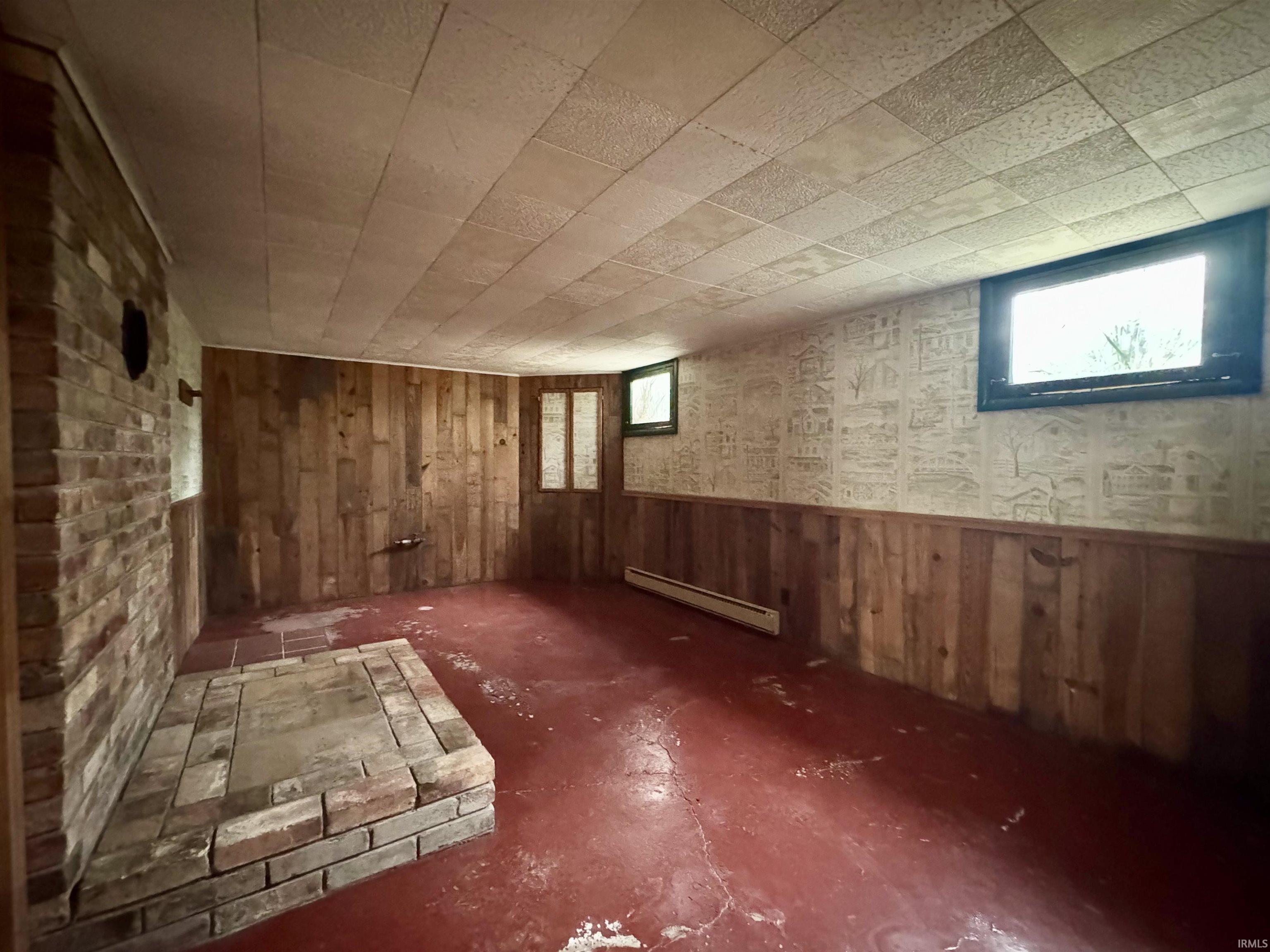 Basement featuring wood walls, healthy amount of natural light, and a baseboard radiator