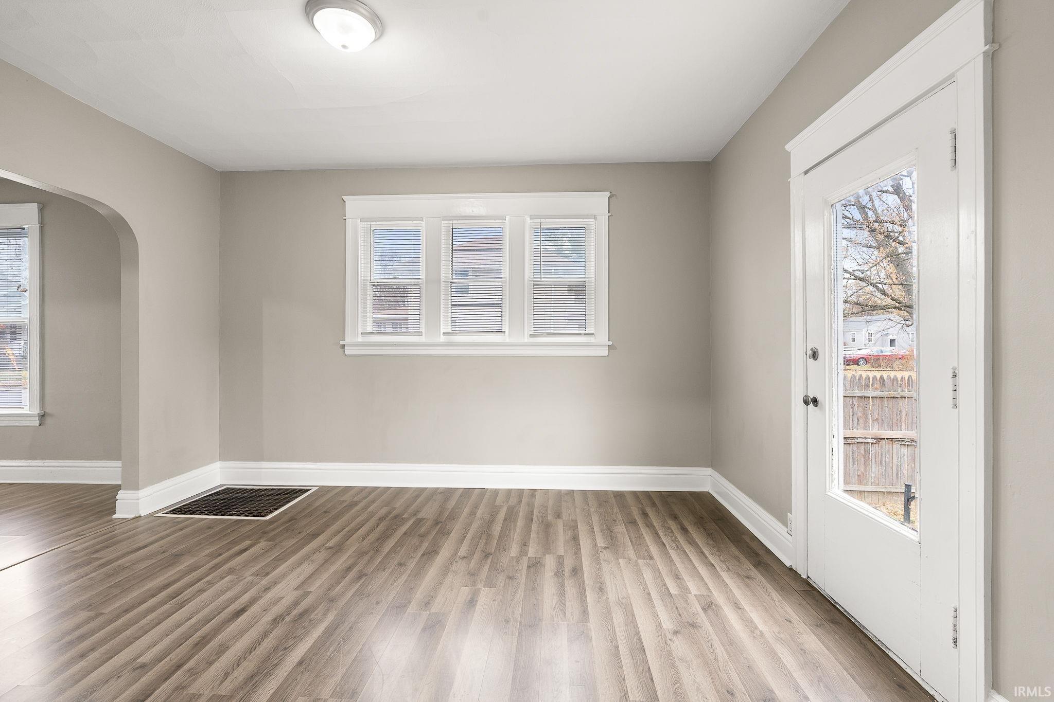 Empty room with arched walkways, plenty of natural light, and light wood-style floors
