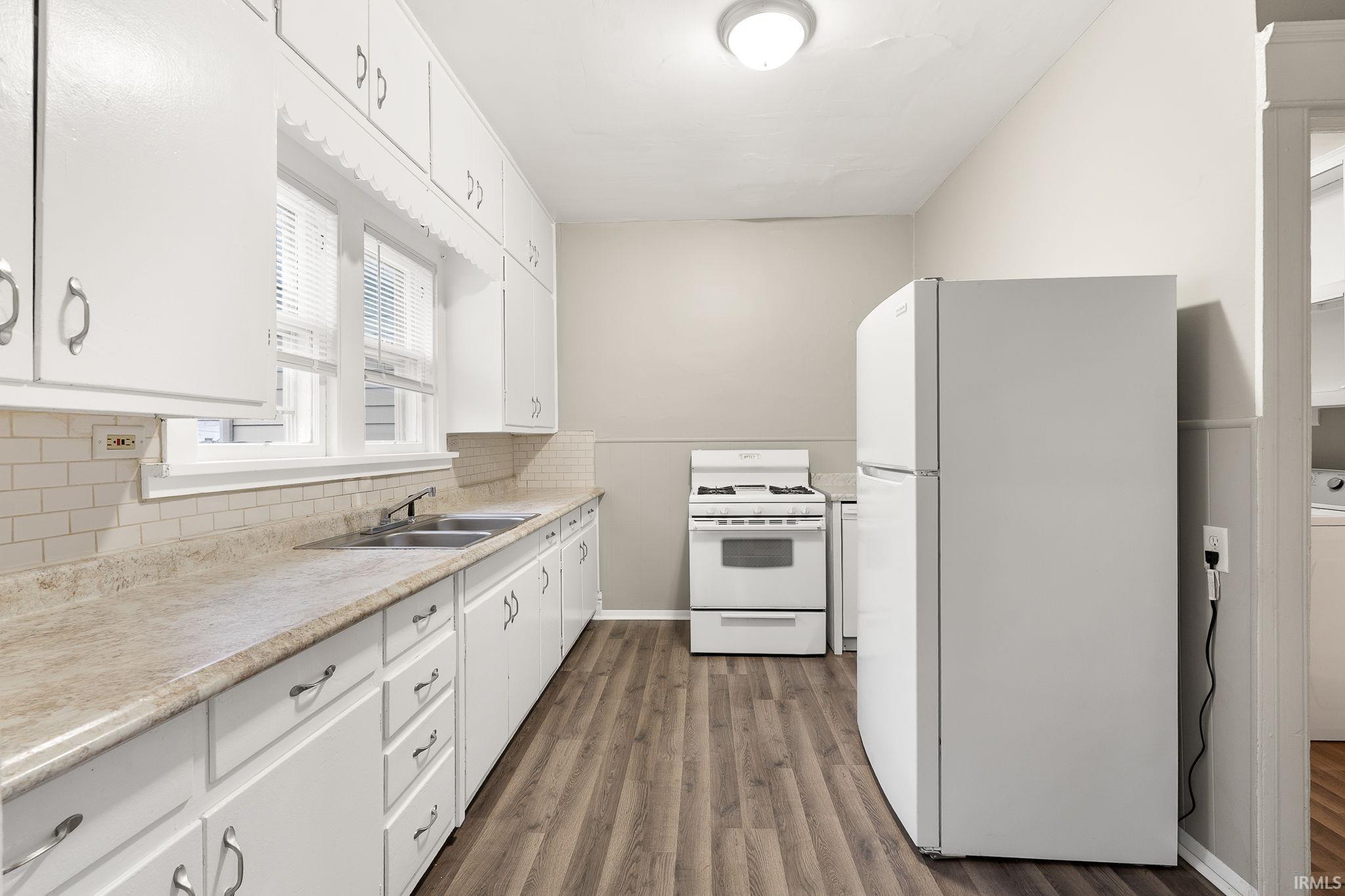 Kitchen with white appliances, light countertops, white cabinetry, dark wood finished floors, and decorative backsplash