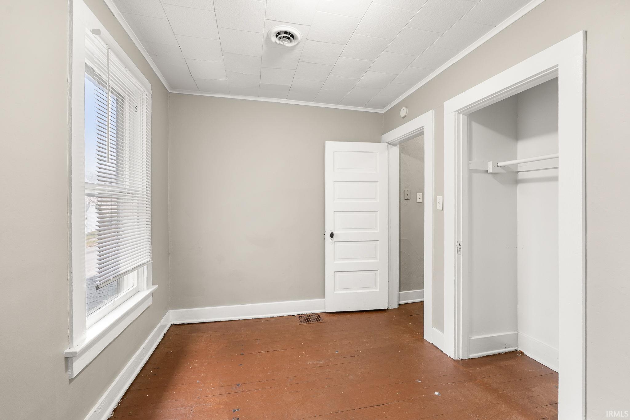 Unfurnished bedroom featuring dark wood-type flooring, ornamental molding, multiple windows, and a closet