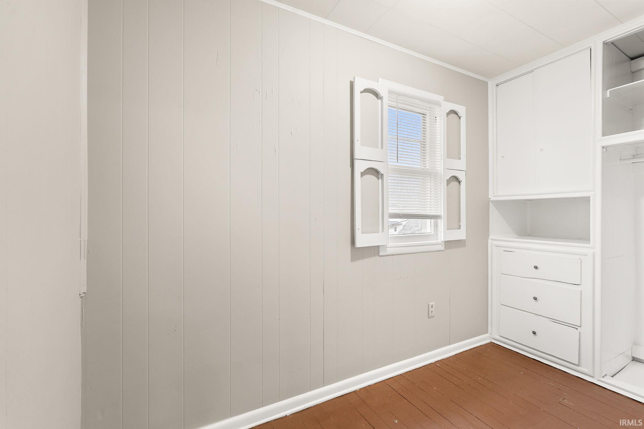 Spare room with wood walls, dark wood-type flooring, and crown molding