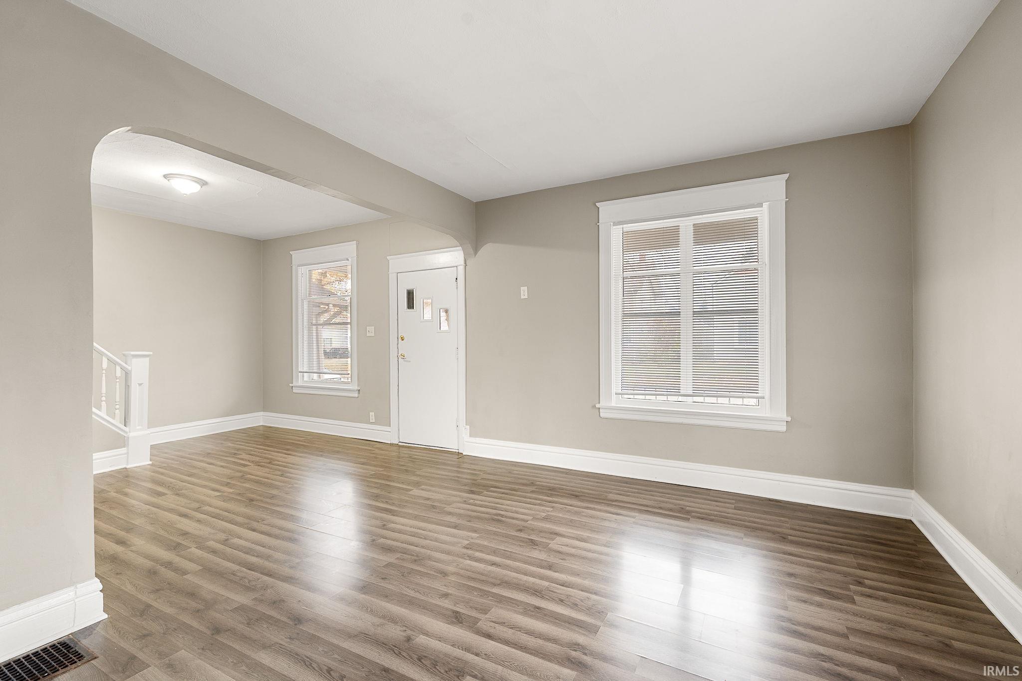 Unfurnished living room featuring arched walkways, wood finished floors, and stairs