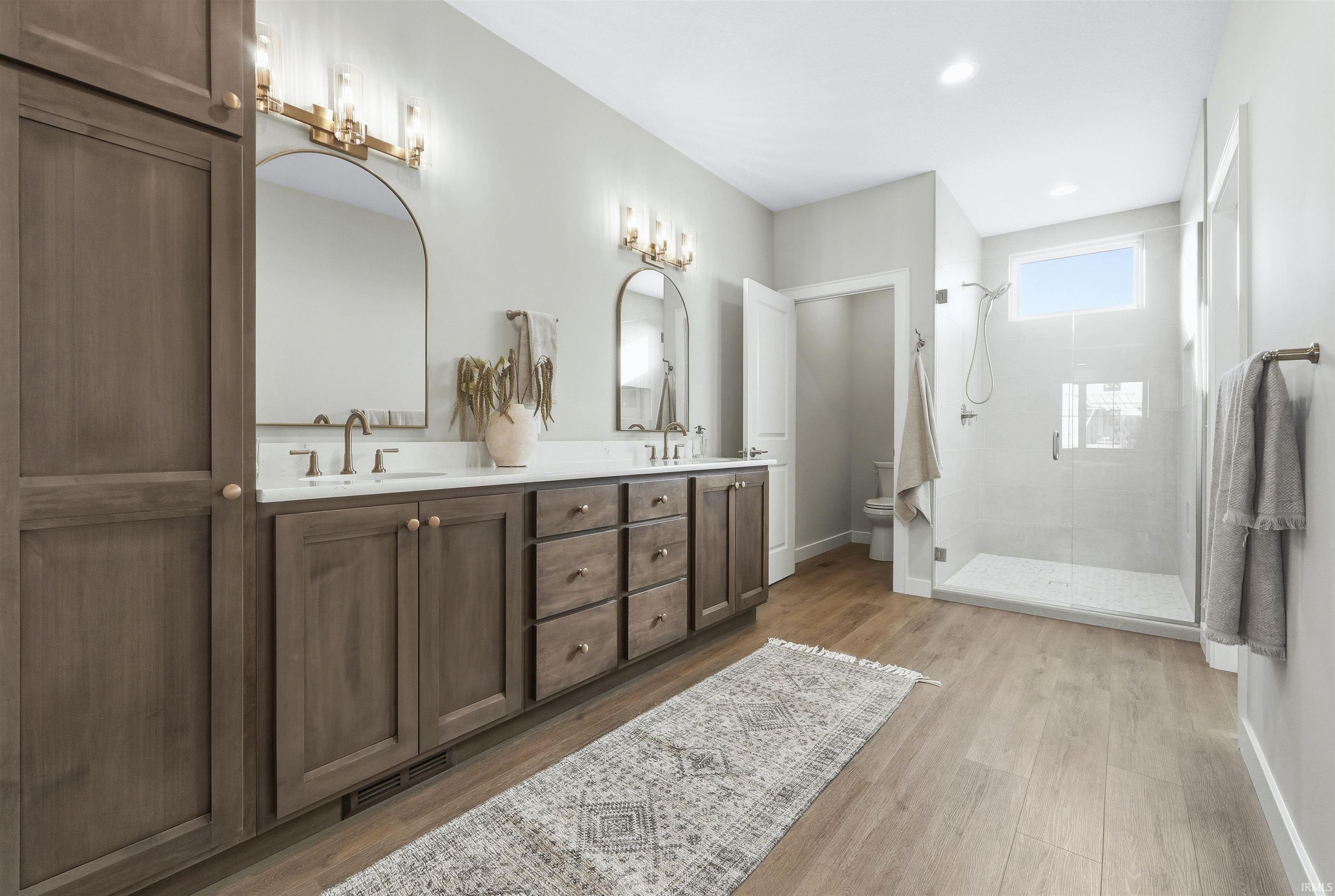 Bathroom with double vanity, a shower stall, and light wood-type flooring