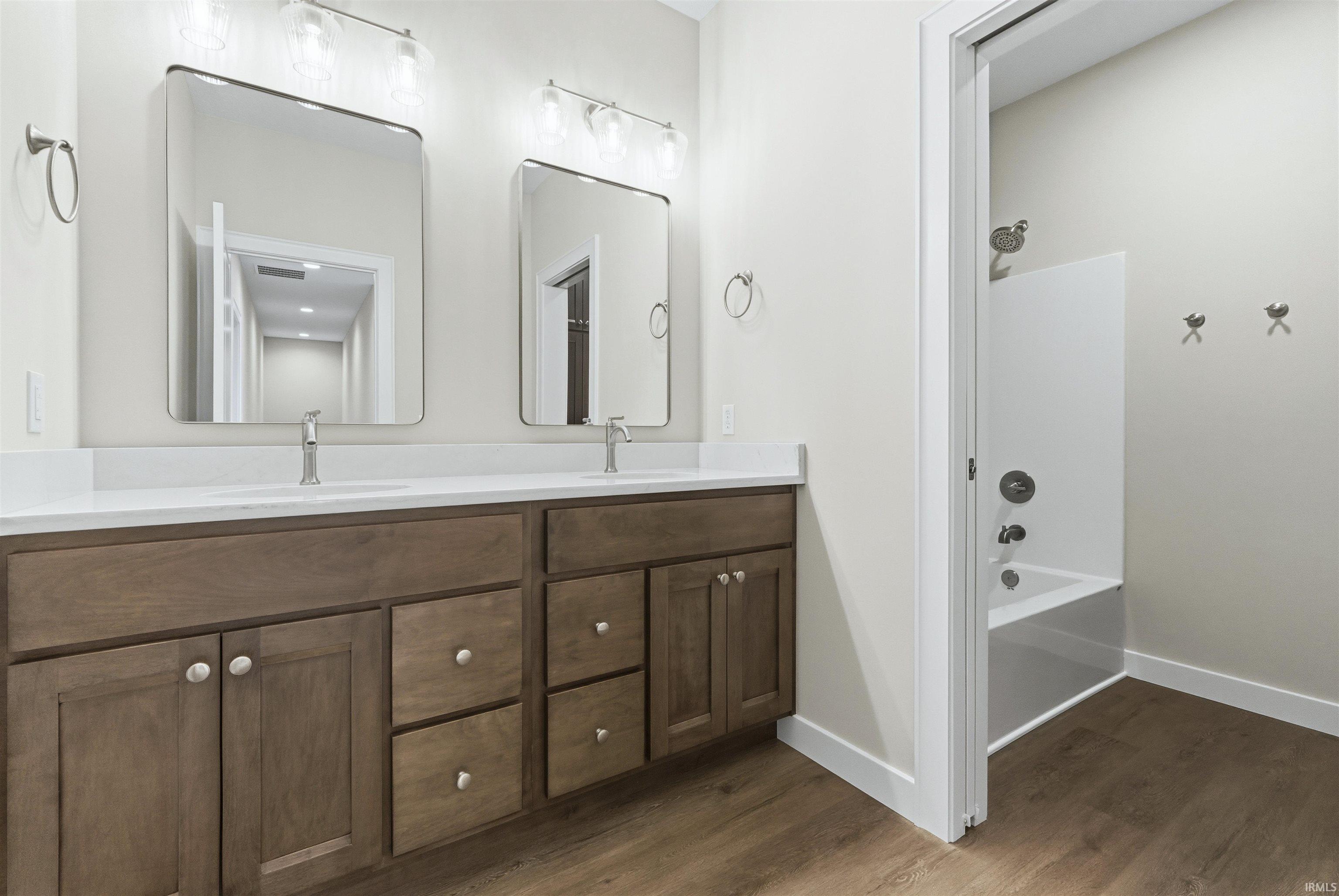 Bathroom featuring shower / tub combination, double vanity, and dark wood-style flooring