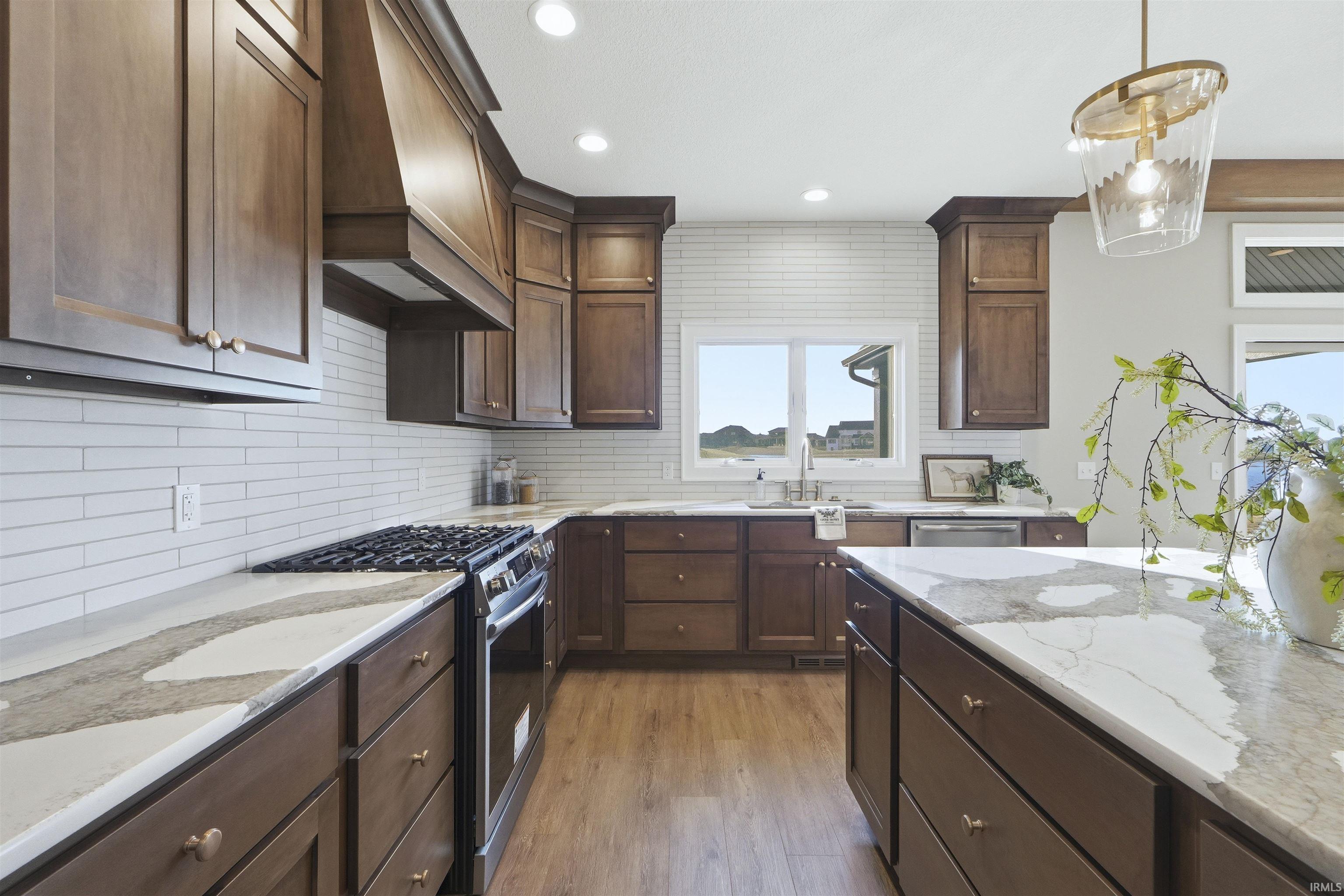 Kitchen featuring appliances with stainless steel finishes, dark brown cabinets, light stone counters, premium range hood, and backsplash