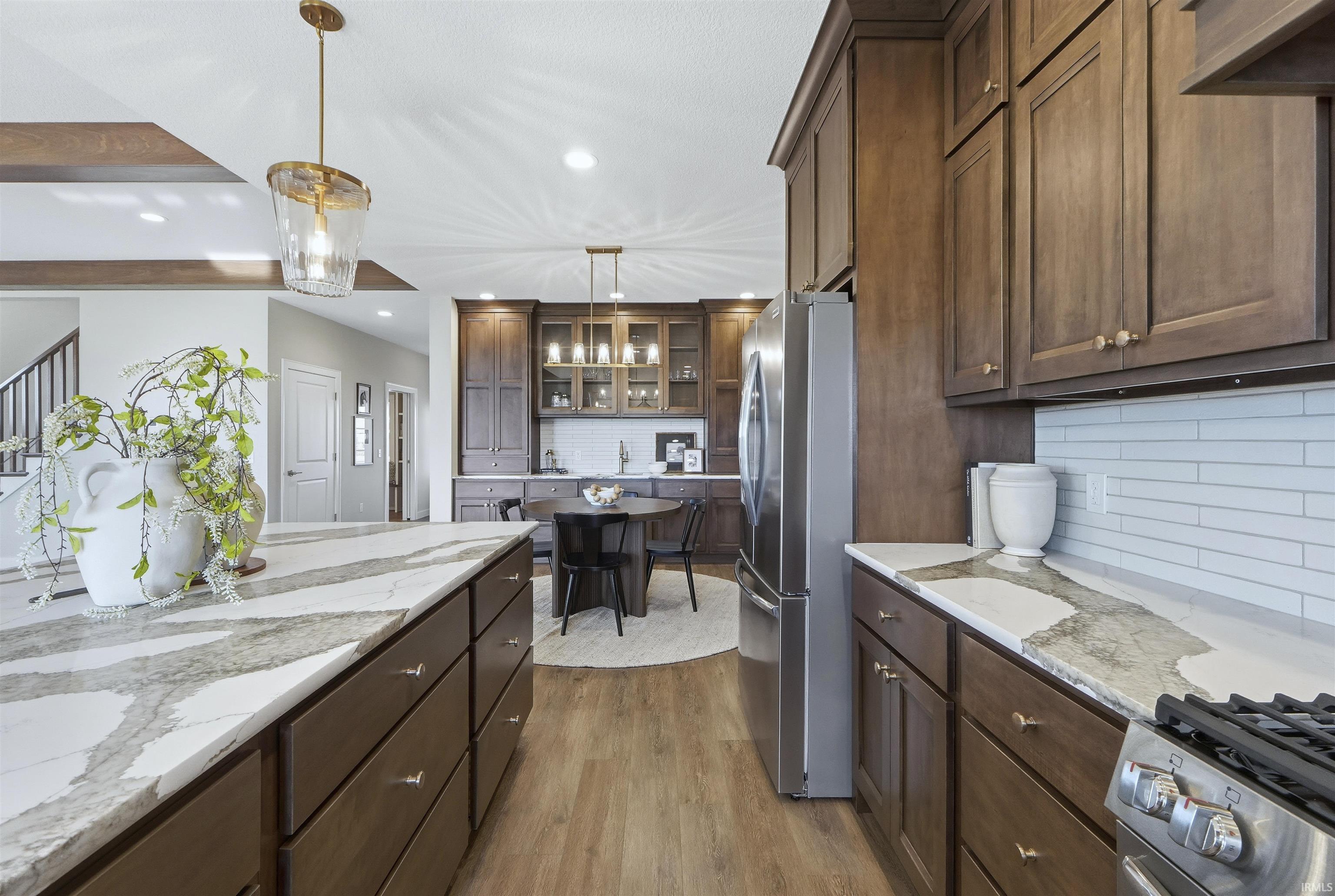 Kitchen with light stone counters, glass insert cabinets, stainless steel appliances, decorative backsplash, and light wood-style flooring
