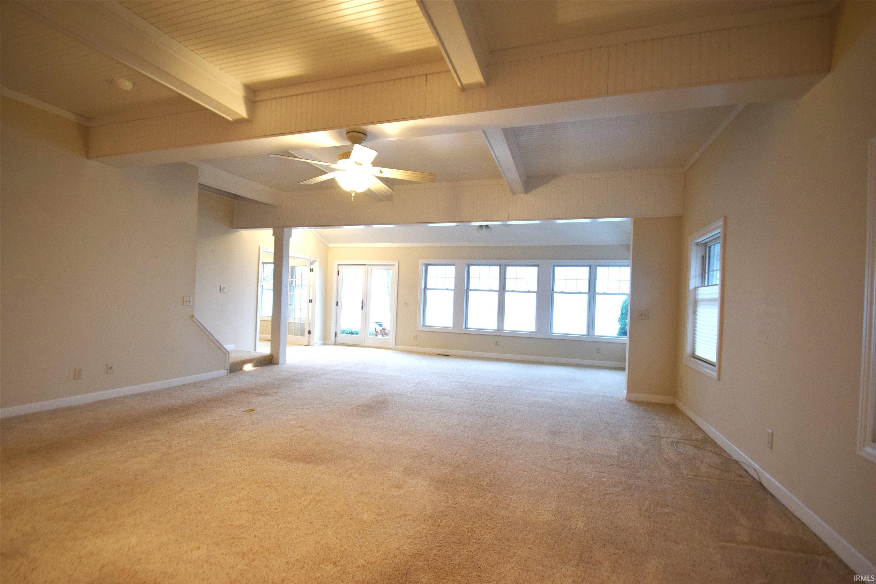 Empty room featuring beam ceiling, ceiling fan, light colored carpet, and crown molding