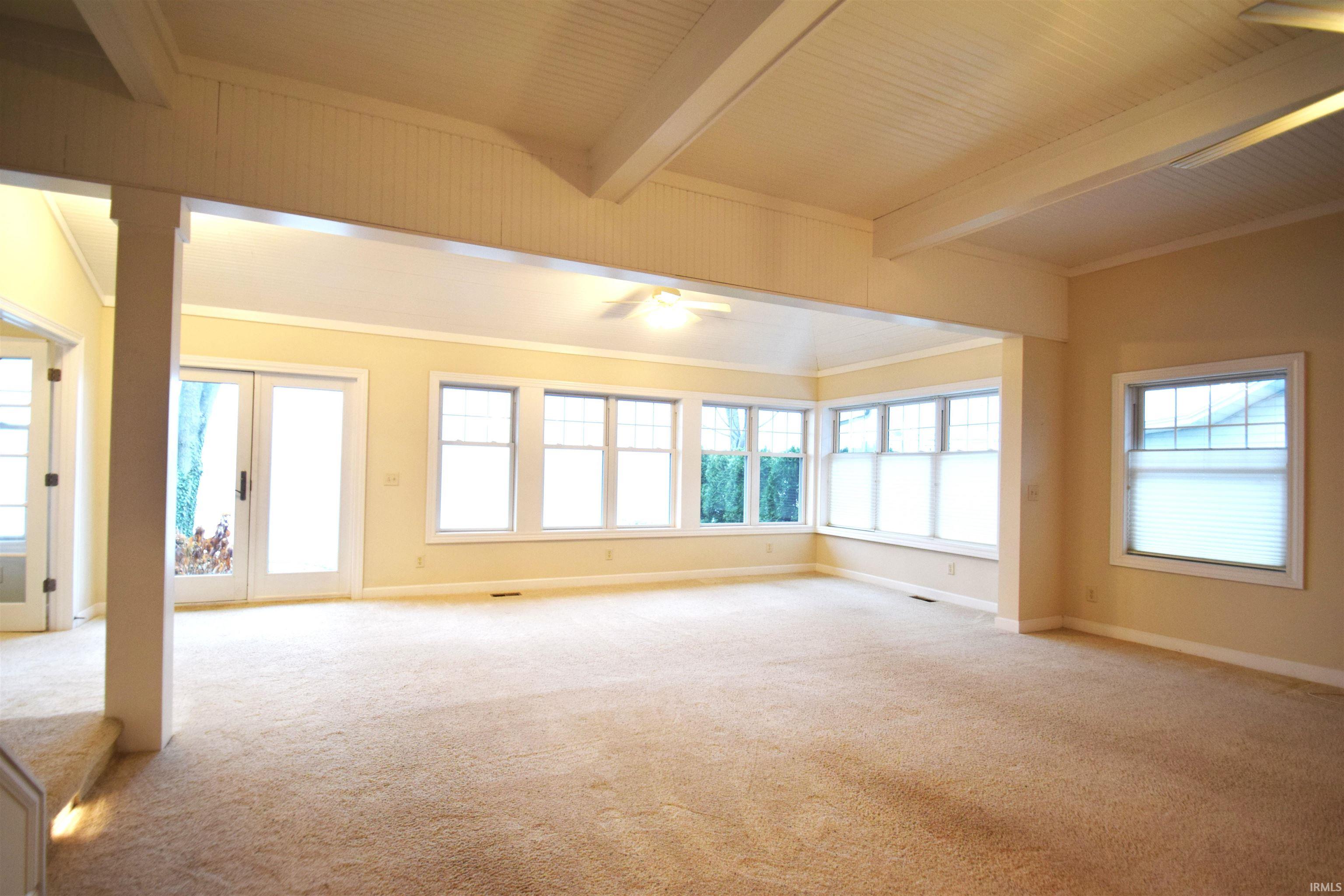 Unfurnished living room featuring crown molding, light carpet, beamed ceiling, plenty of natural light, and a ceiling fan