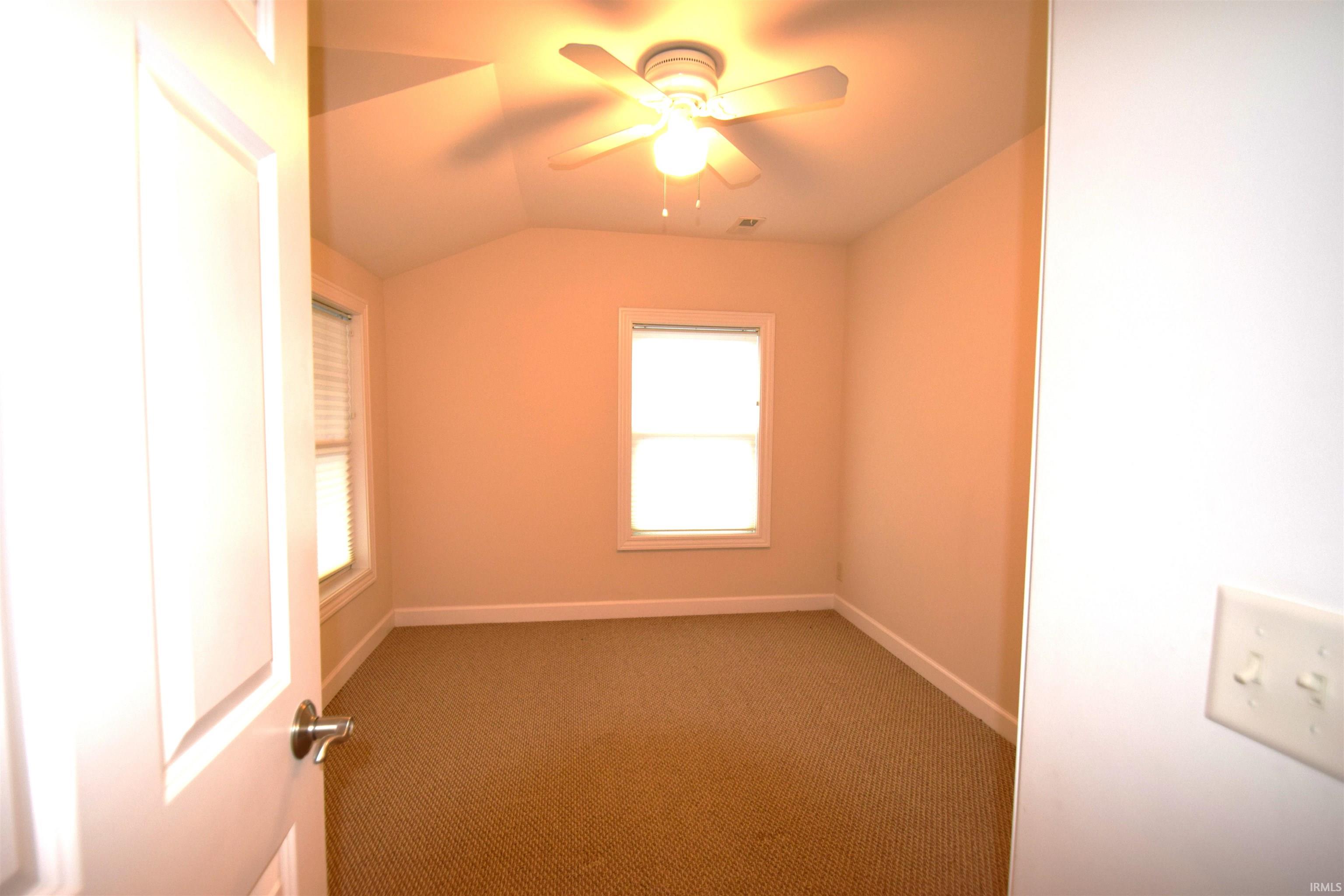 Empty room with vaulted ceiling, carpet, and ceiling fan