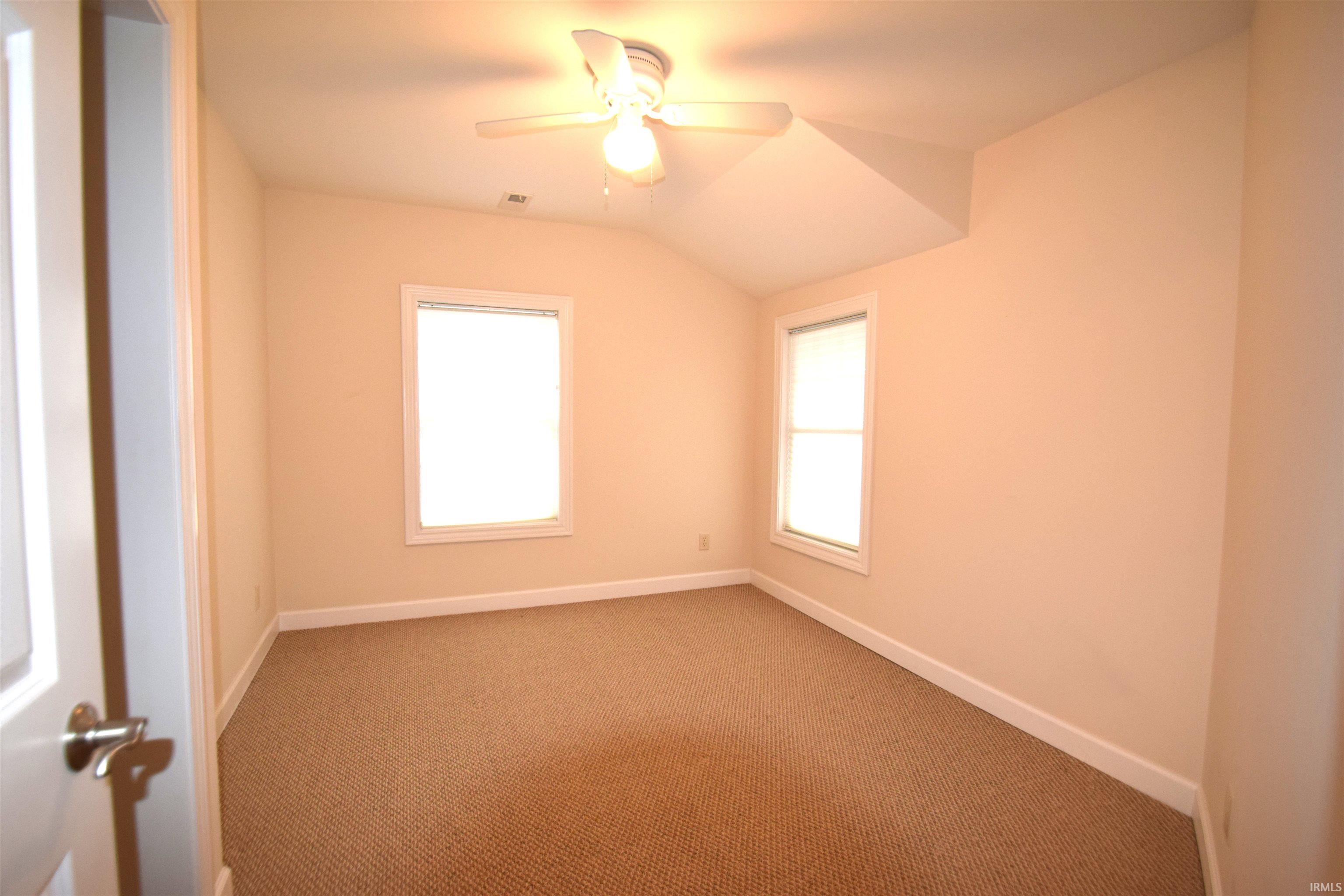 Carpeted empty room featuring vaulted ceiling, plenty of natural light, and a ceiling fan