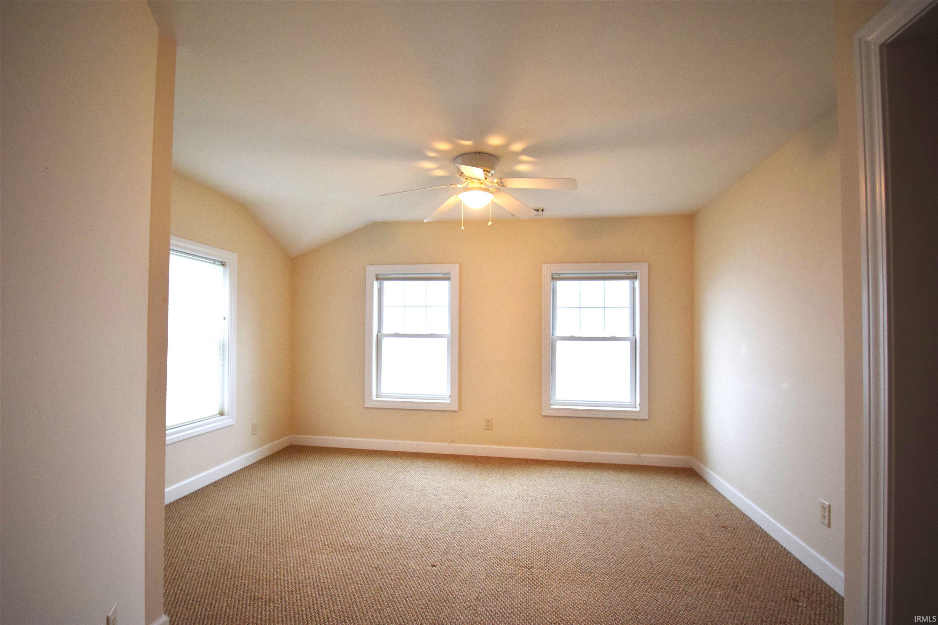 Unfurnished room featuring lofted ceiling, light colored carpet, and a ceiling fan