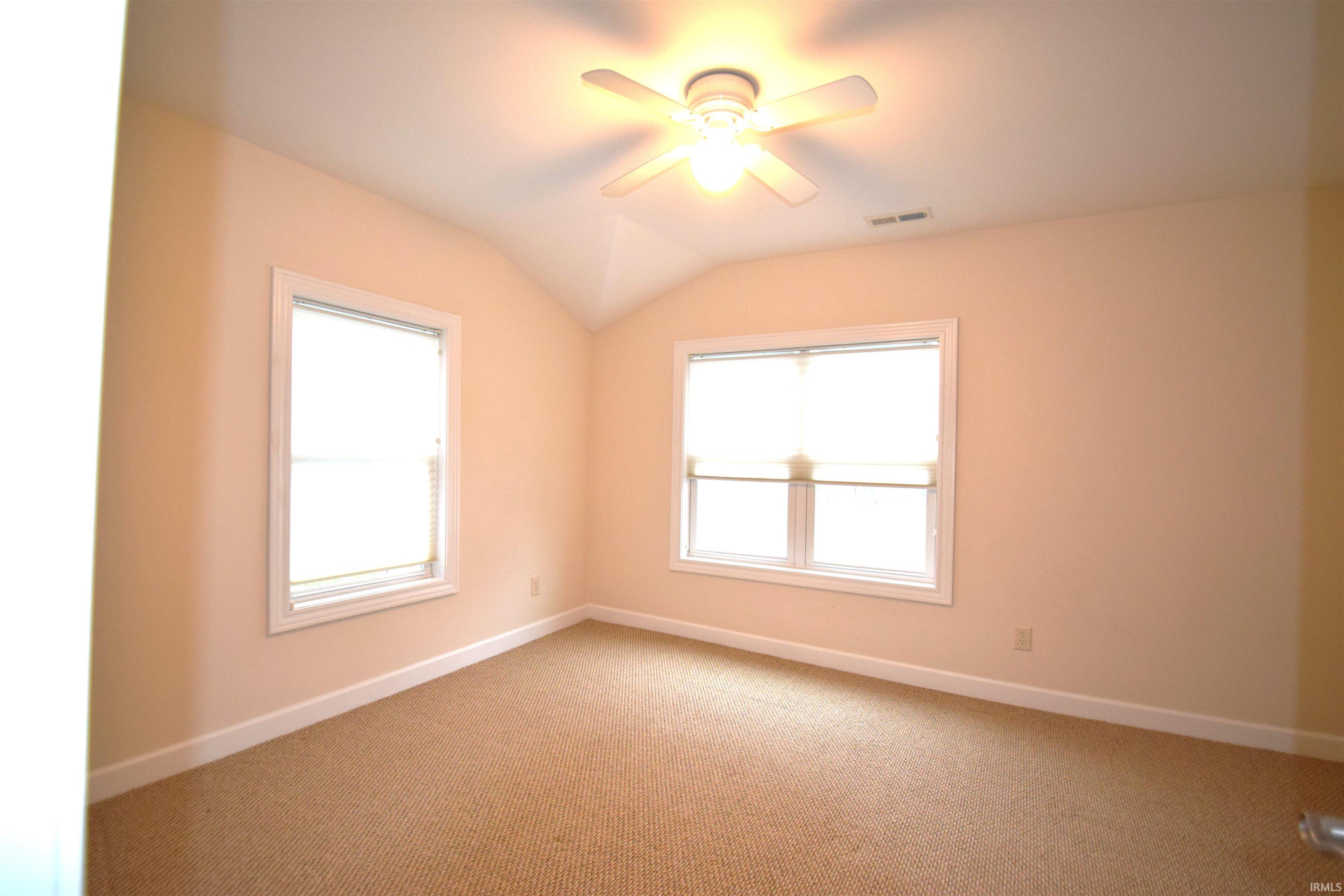 Carpeted spare room featuring lofted ceiling and ceiling fan