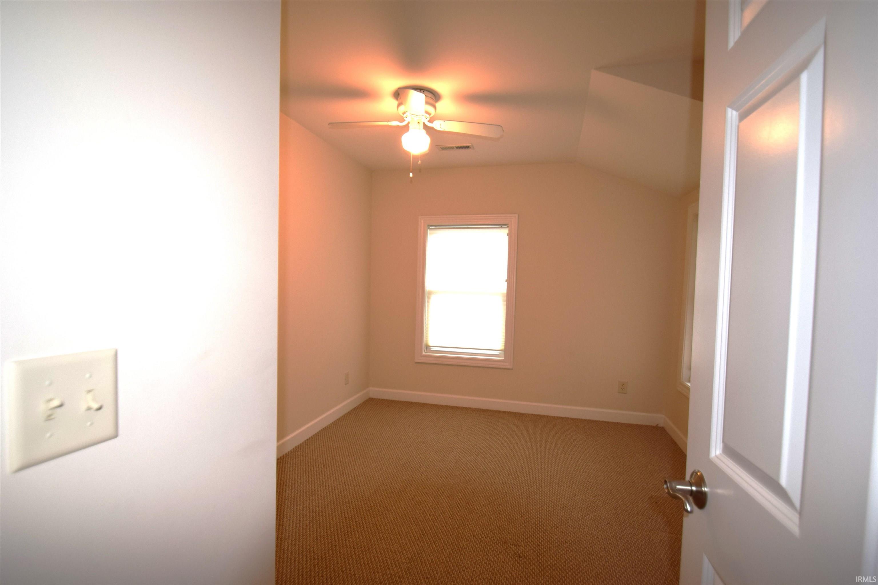 Carpeted spare room with vaulted ceiling and a ceiling fan