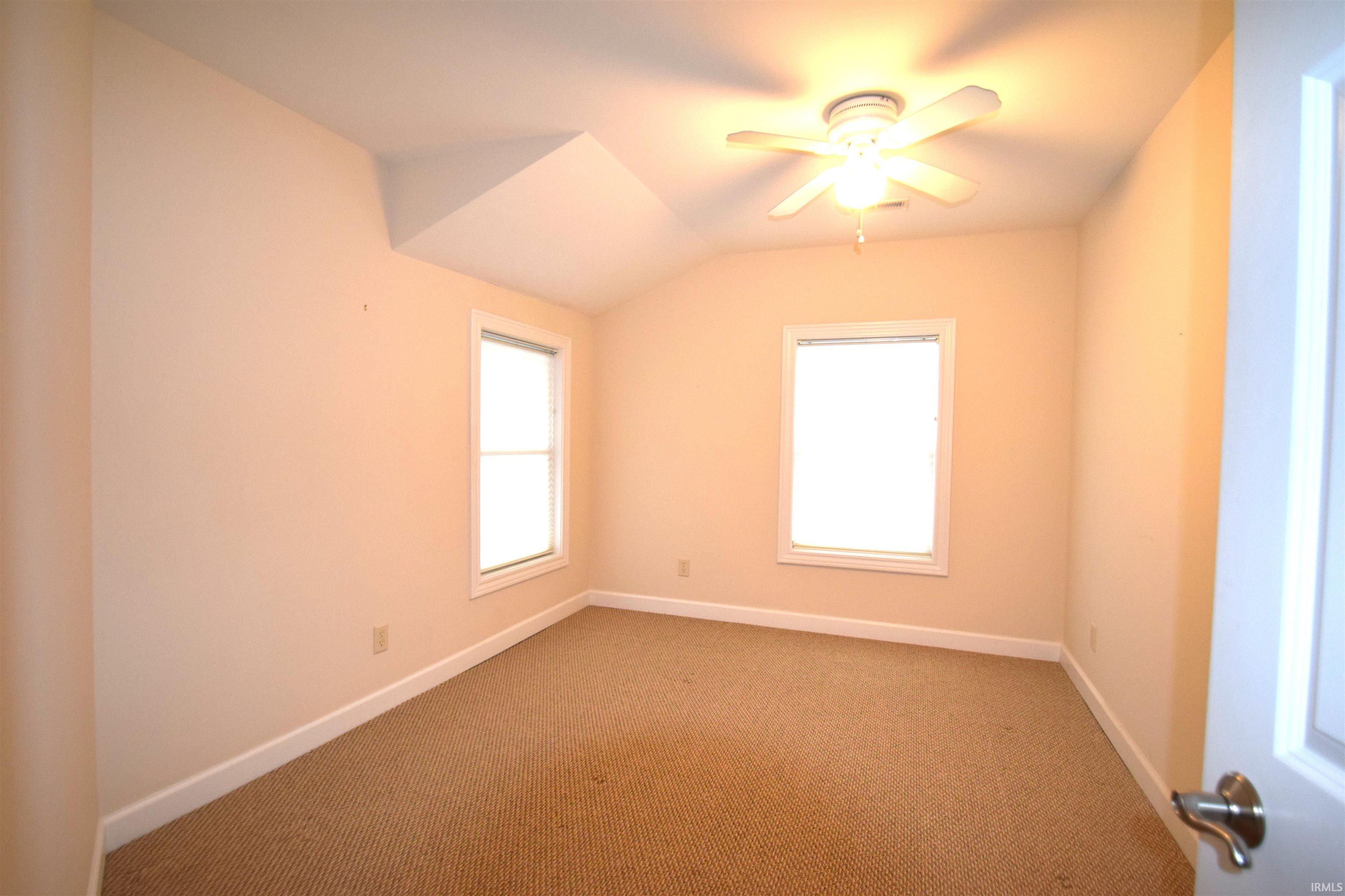 Empty room with vaulted ceiling, ceiling fan, and carpet floors