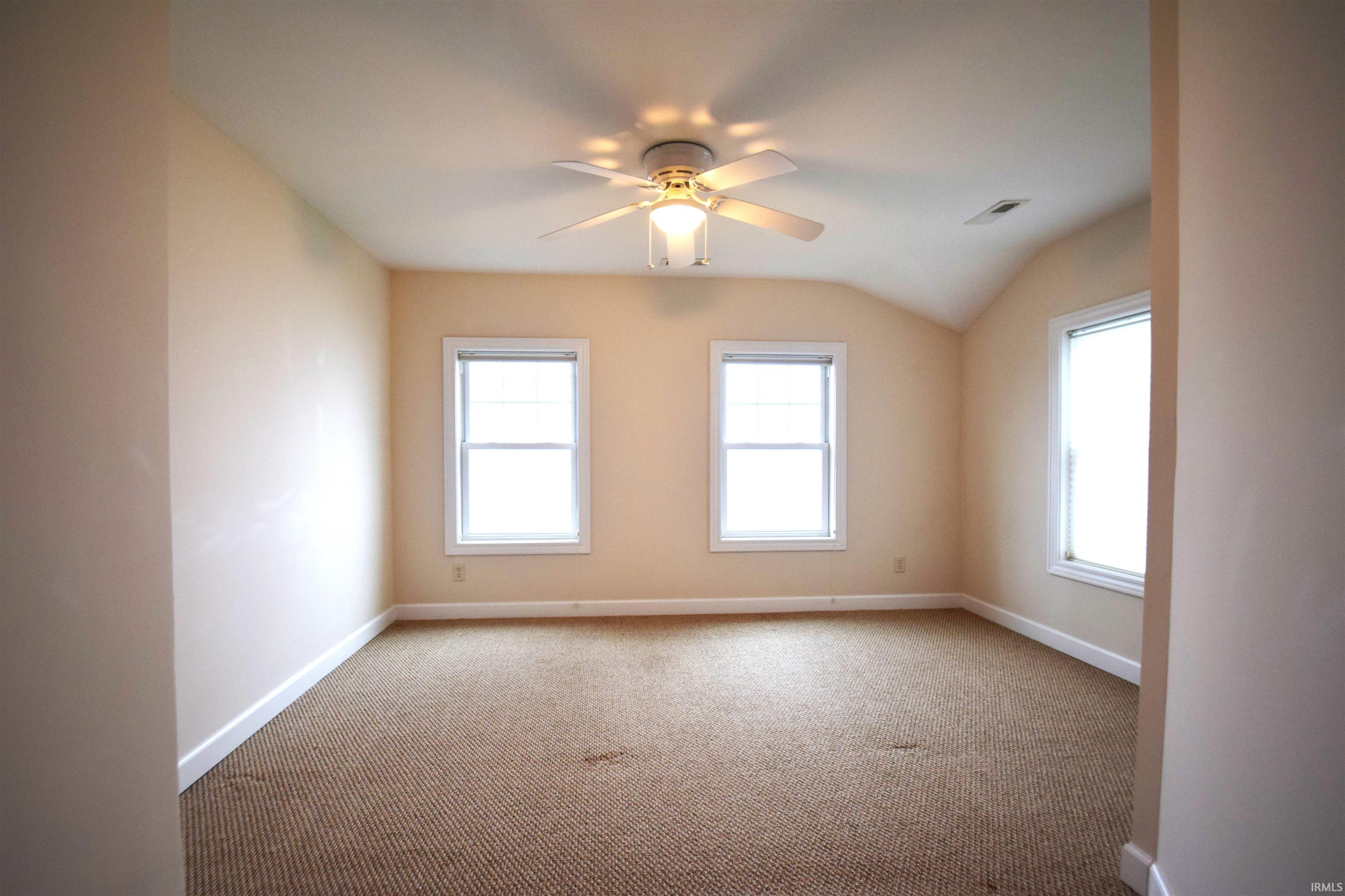 Spare room with carpet flooring, vaulted ceiling, and ceiling fan