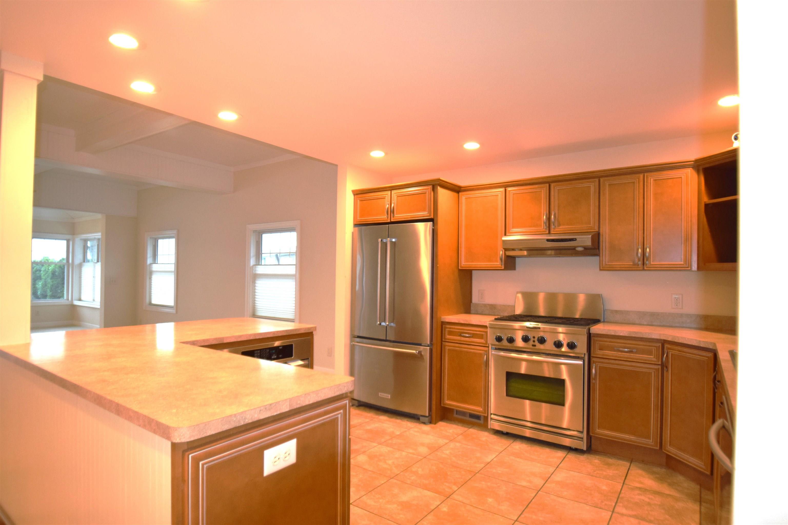 Kitchen with open shelves, stainless steel appliances, recessed lighting, light countertops, and brown cabinetry