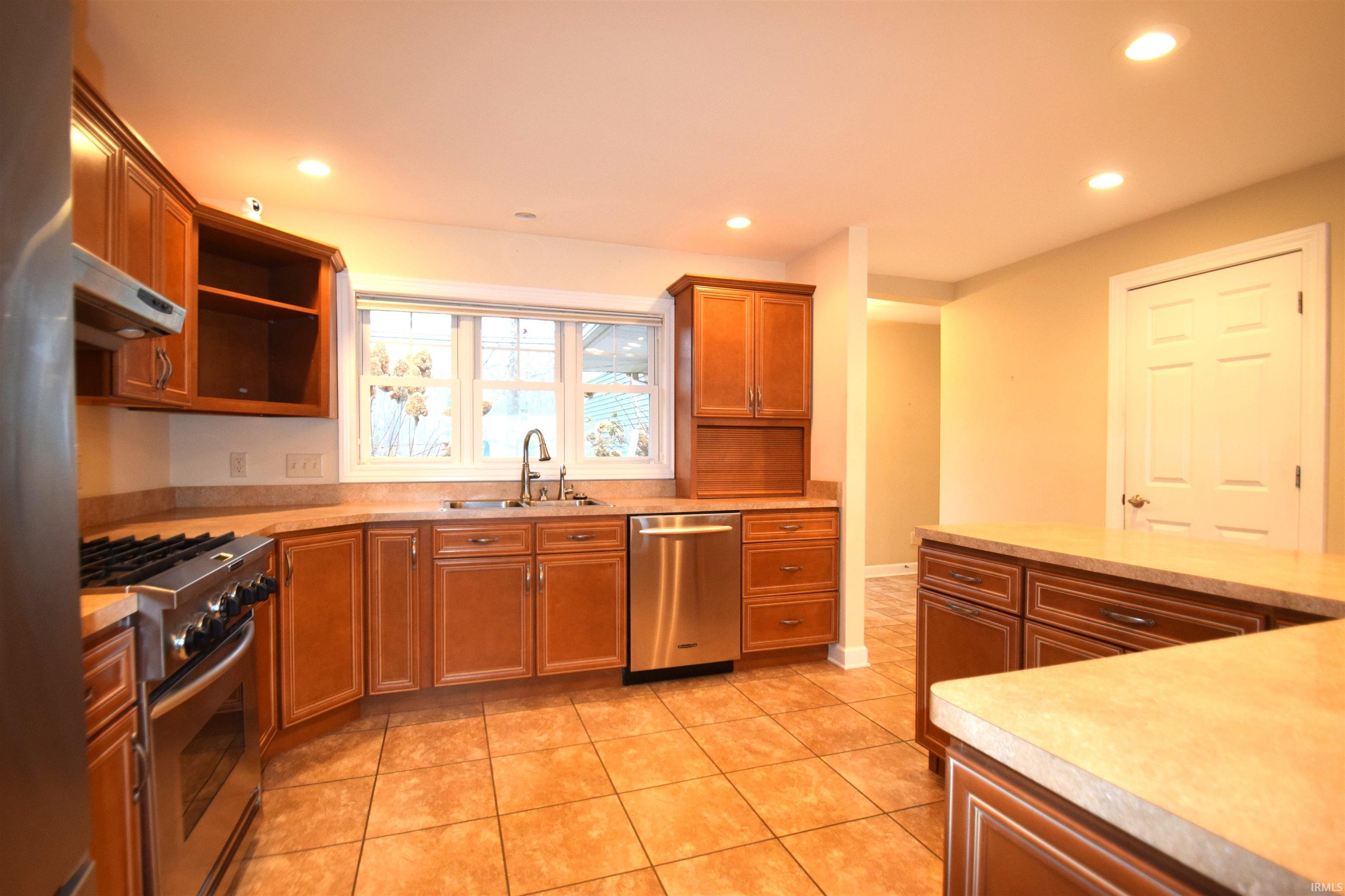 Kitchen featuring stainless steel appliances, brown cabinetry, light countertops, recessed lighting, and under cabinet range hood