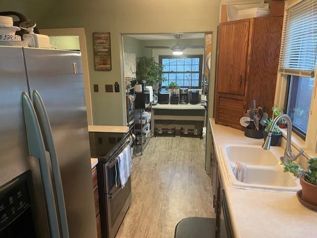 Kitchen featuring stainless steel appliances, light wood-type flooring, light countertops, brown cabinetry, and ceiling fan