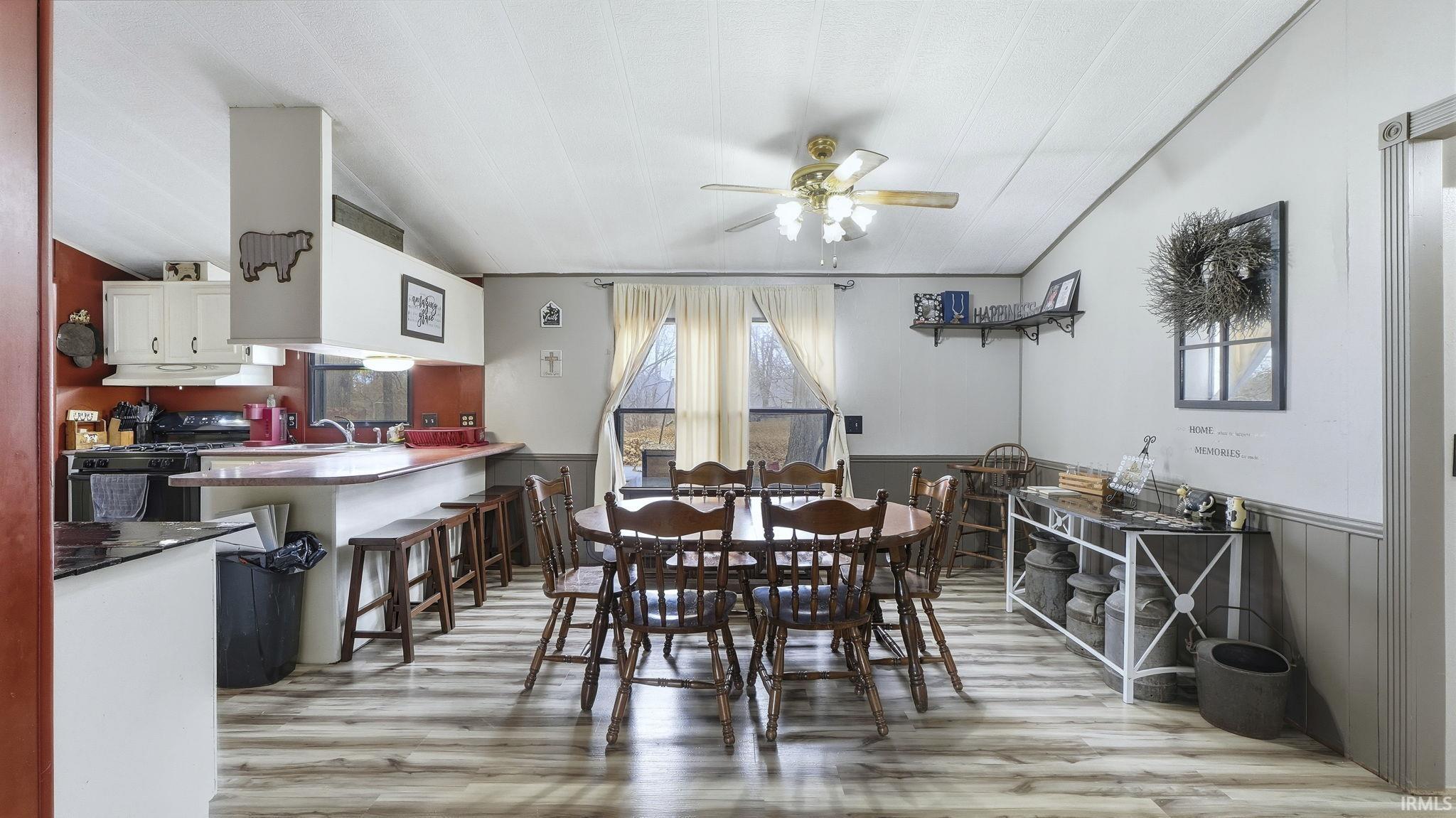 Dining area featuring wainscoting, ceiling fan, light wood-style floors, and vaulted ceiling