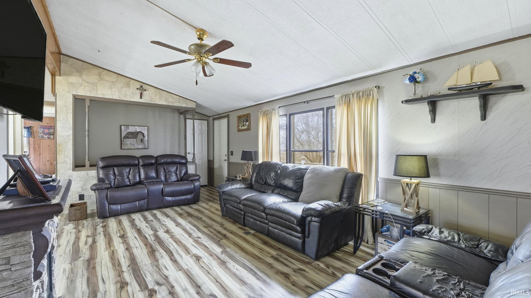 Living area with wood finished floors, wainscoting, vaulted ceiling, wooden walls, and ceiling fan