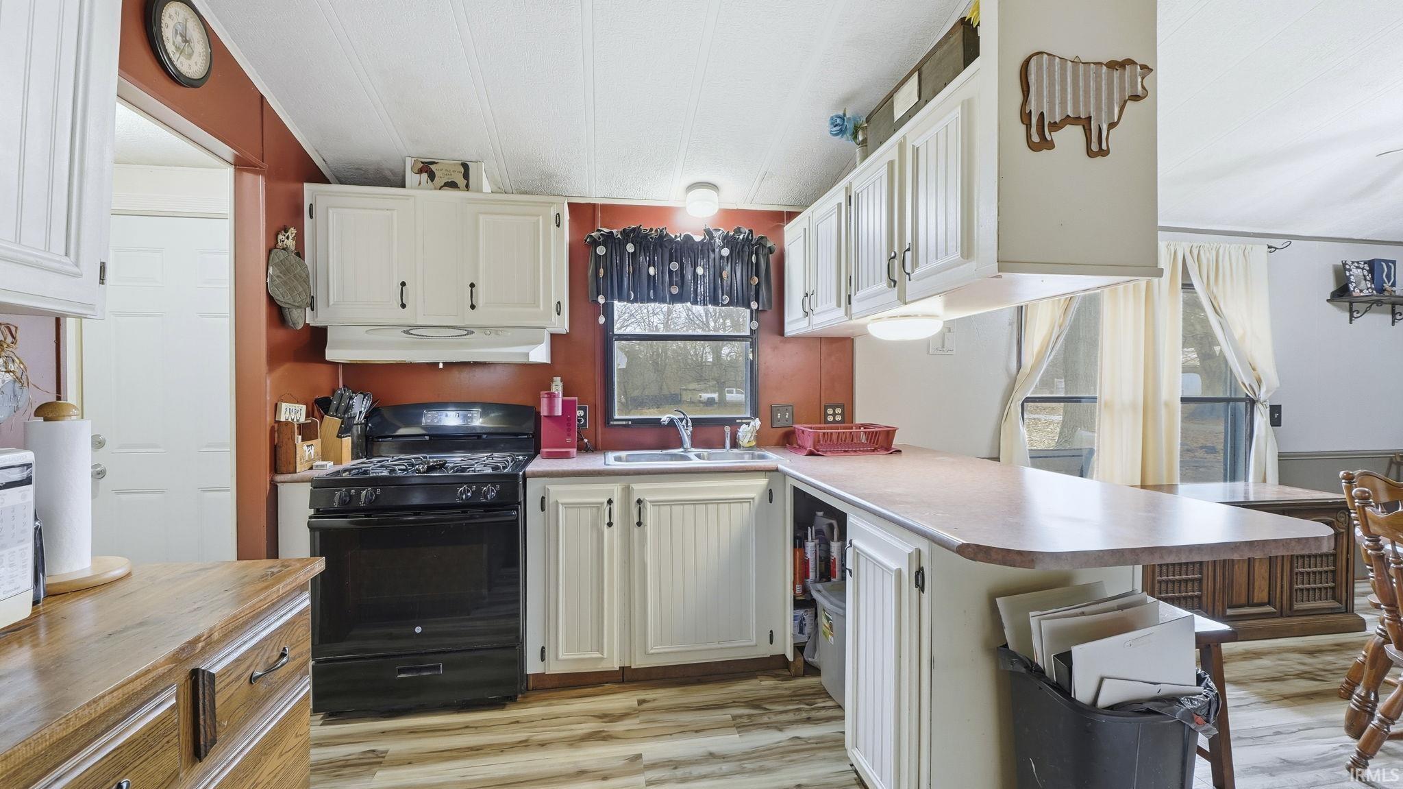 Kitchen featuring black gas range oven, a peninsula, light wood finished floors, under cabinet range hood, and light countertops