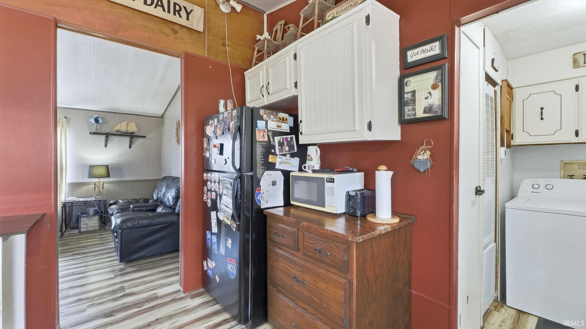 Kitchen with washer / dryer, white microwave, light wood-style flooring, white cabinets, and dark countertops