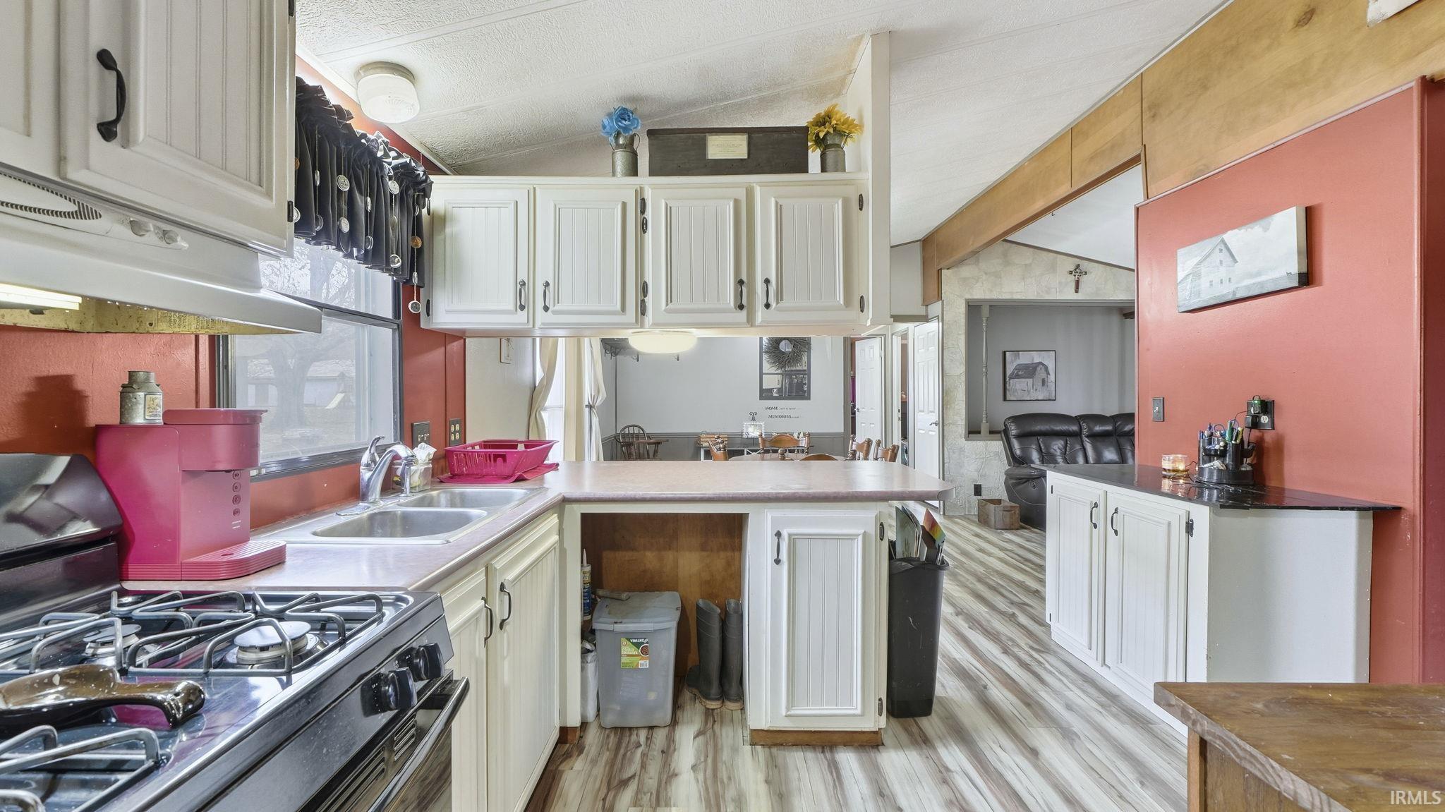 Kitchen with gas stove, vaulted ceiling, a peninsula, white cabinetry, and light wood-type flooring
