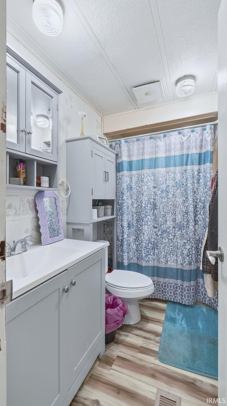Bathroom featuring a textured ceiling, a shower with shower curtain, vanity, and light wood finished floors