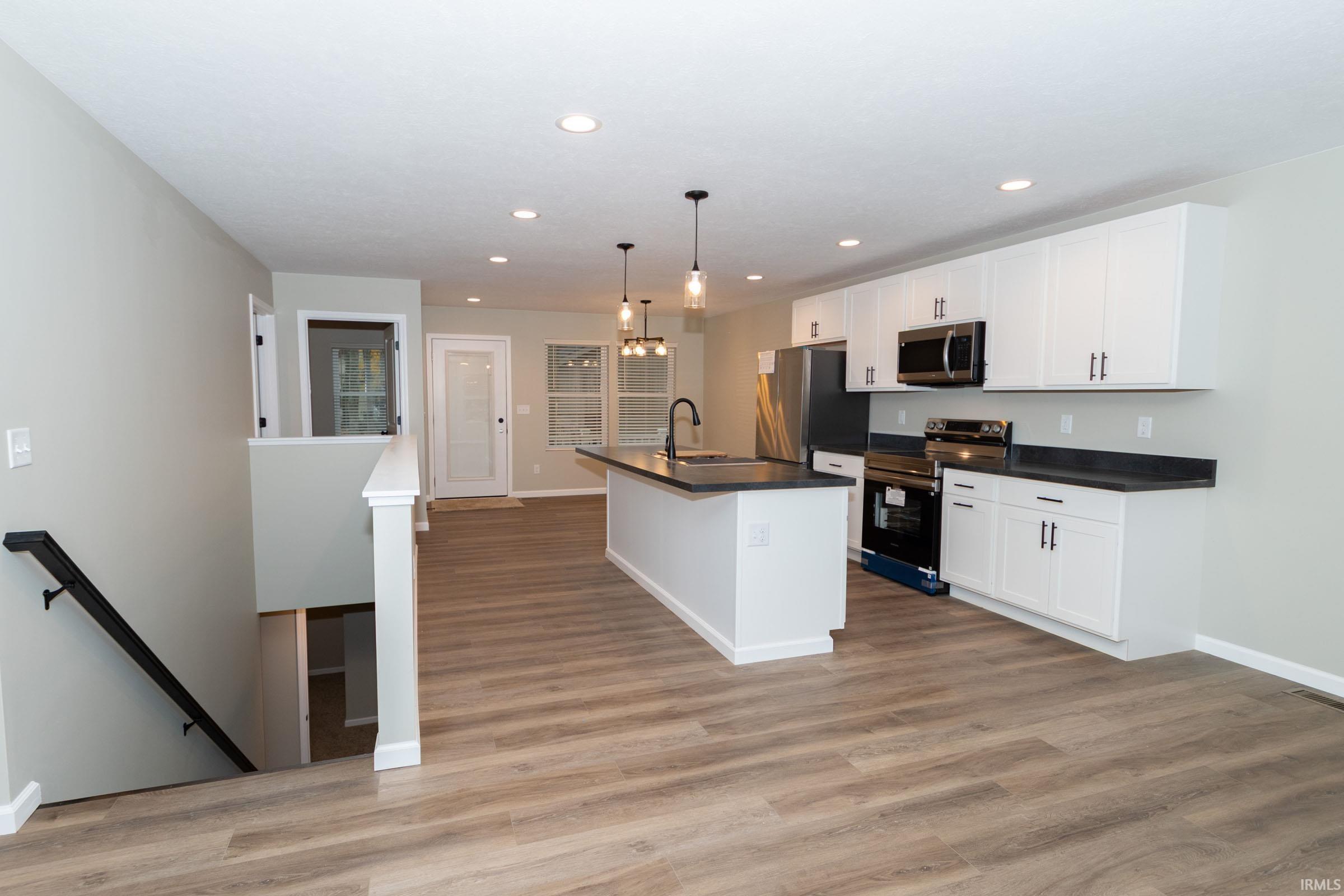 Kitchen featuring dark countertops, a kitchen island with sink, stainless steel appliances, hanging light fixtures, and recessed lighting