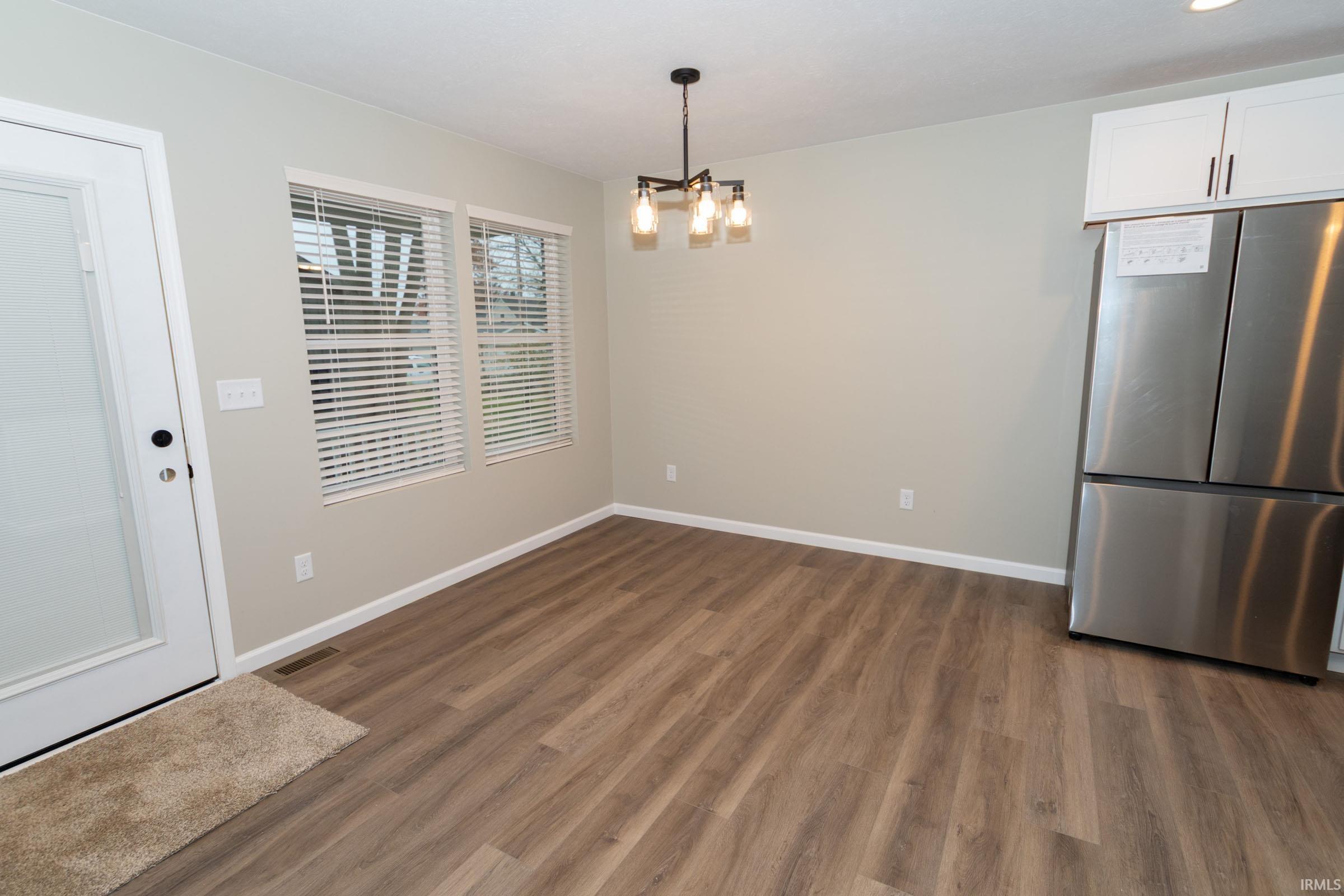 Unfurnished dining area with dark wood-style flooring and a chandelier