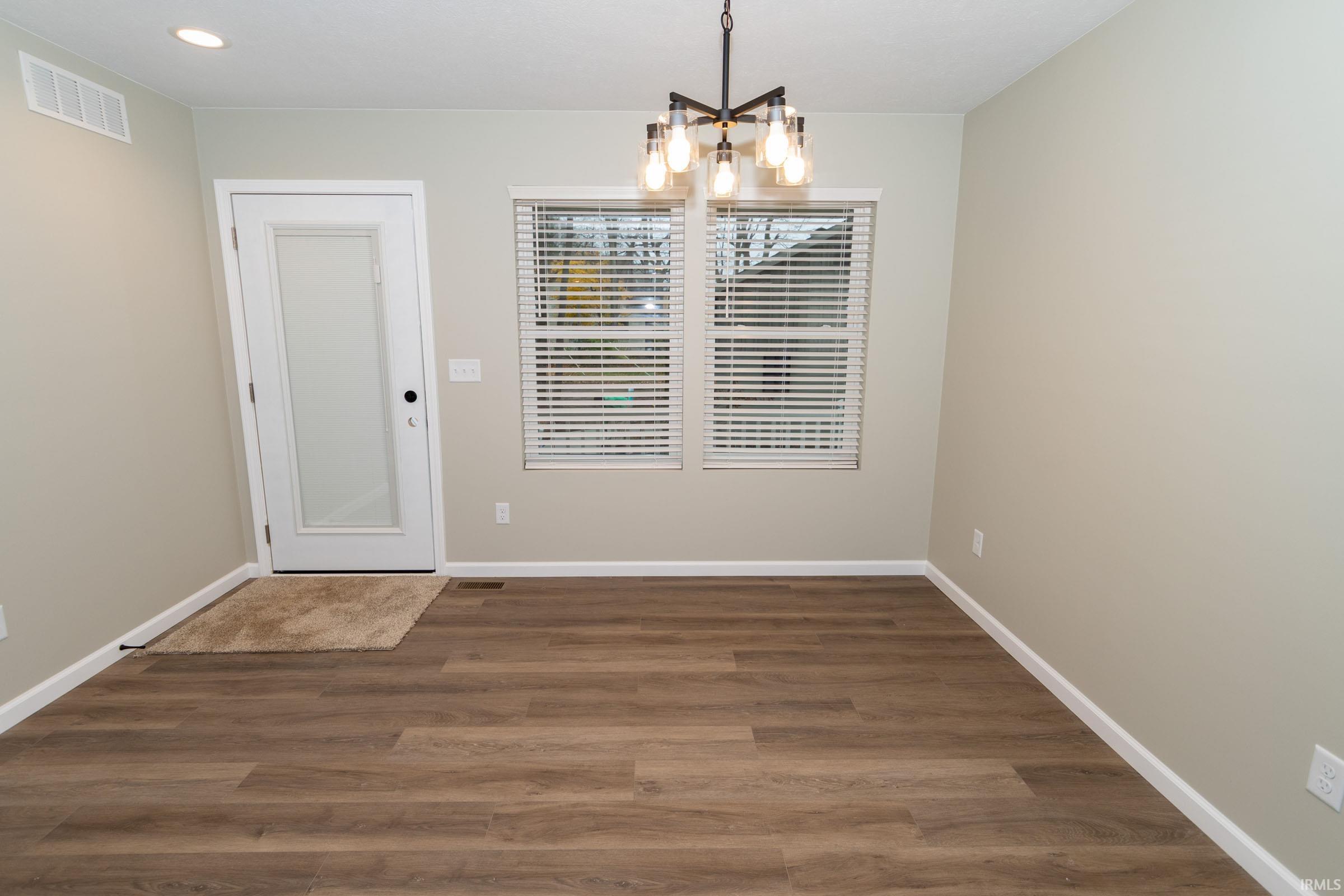 Unfurnished dining area with a chandelier and dark wood-style flooring