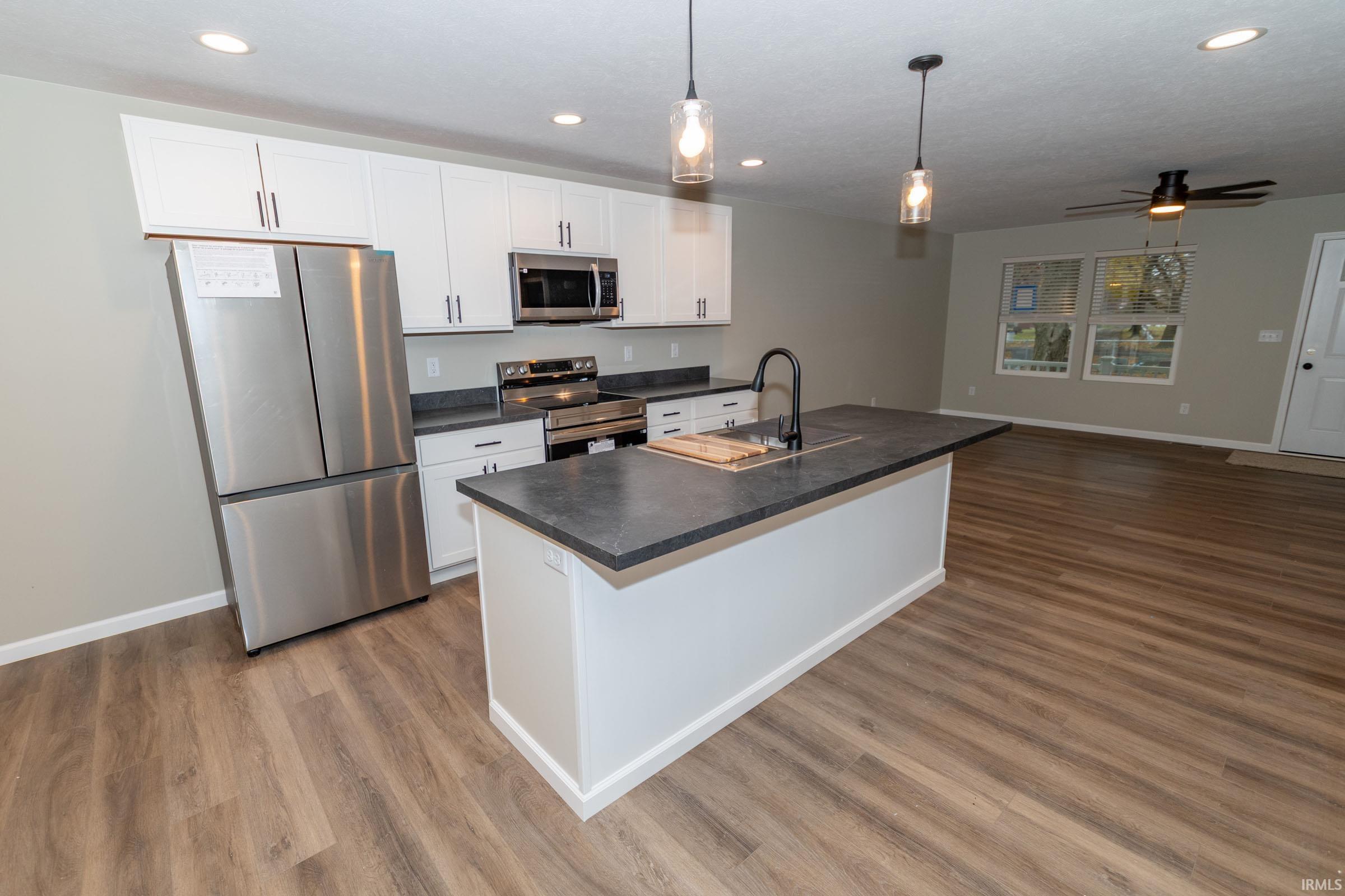 Kitchen featuring appliances with stainless steel finishes, white cabinets, ceiling fan, open floor plan, and recessed lighting