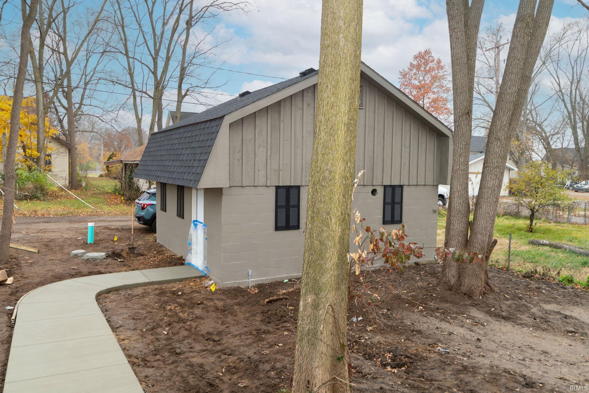 View of property exterior with concrete block siding, a shingled roof, and a gambrel roof