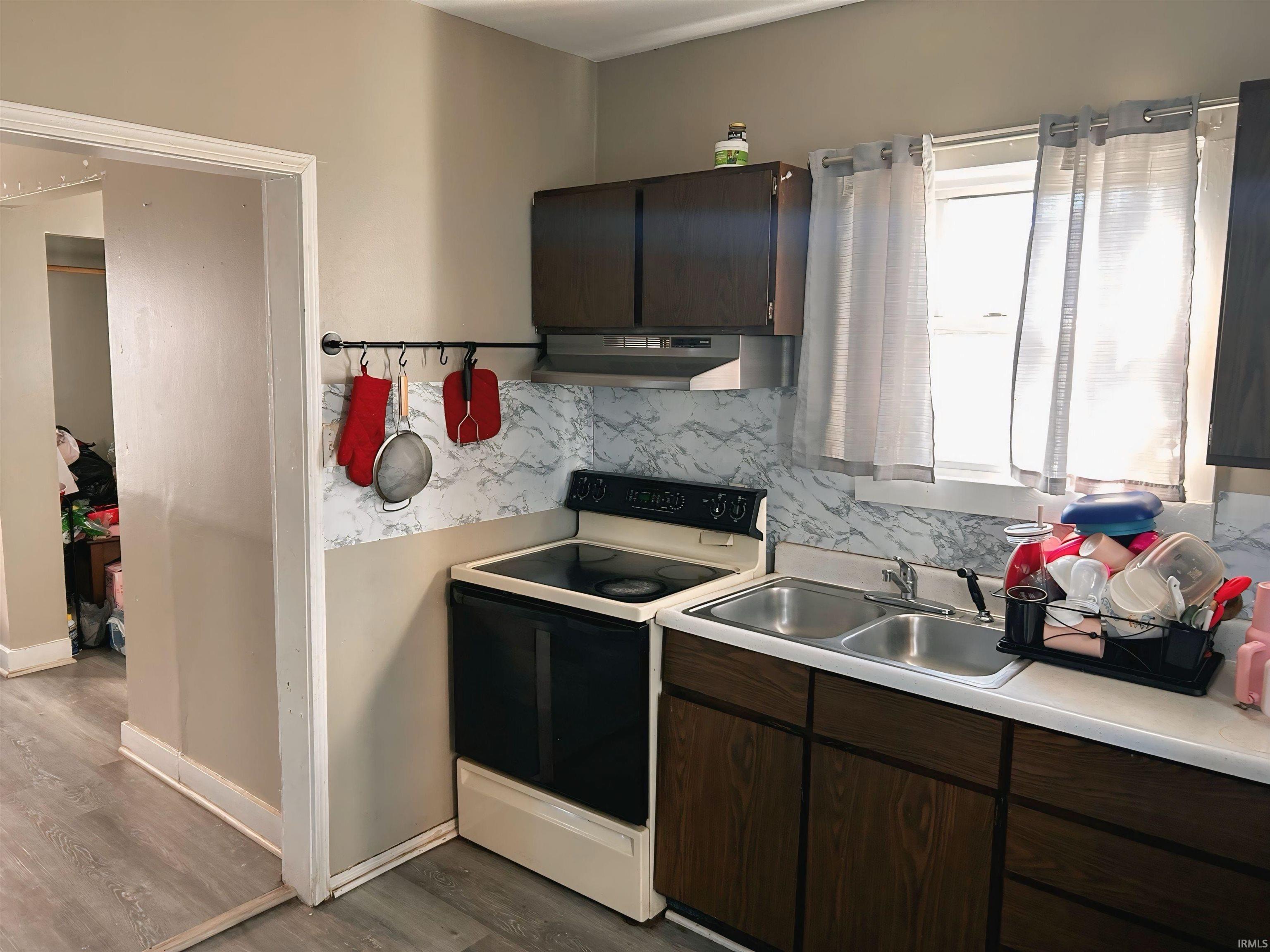 Kitchen featuring electric stove, dark brown cabinets, light countertops, under cabinet range hood, and tasteful backsplash