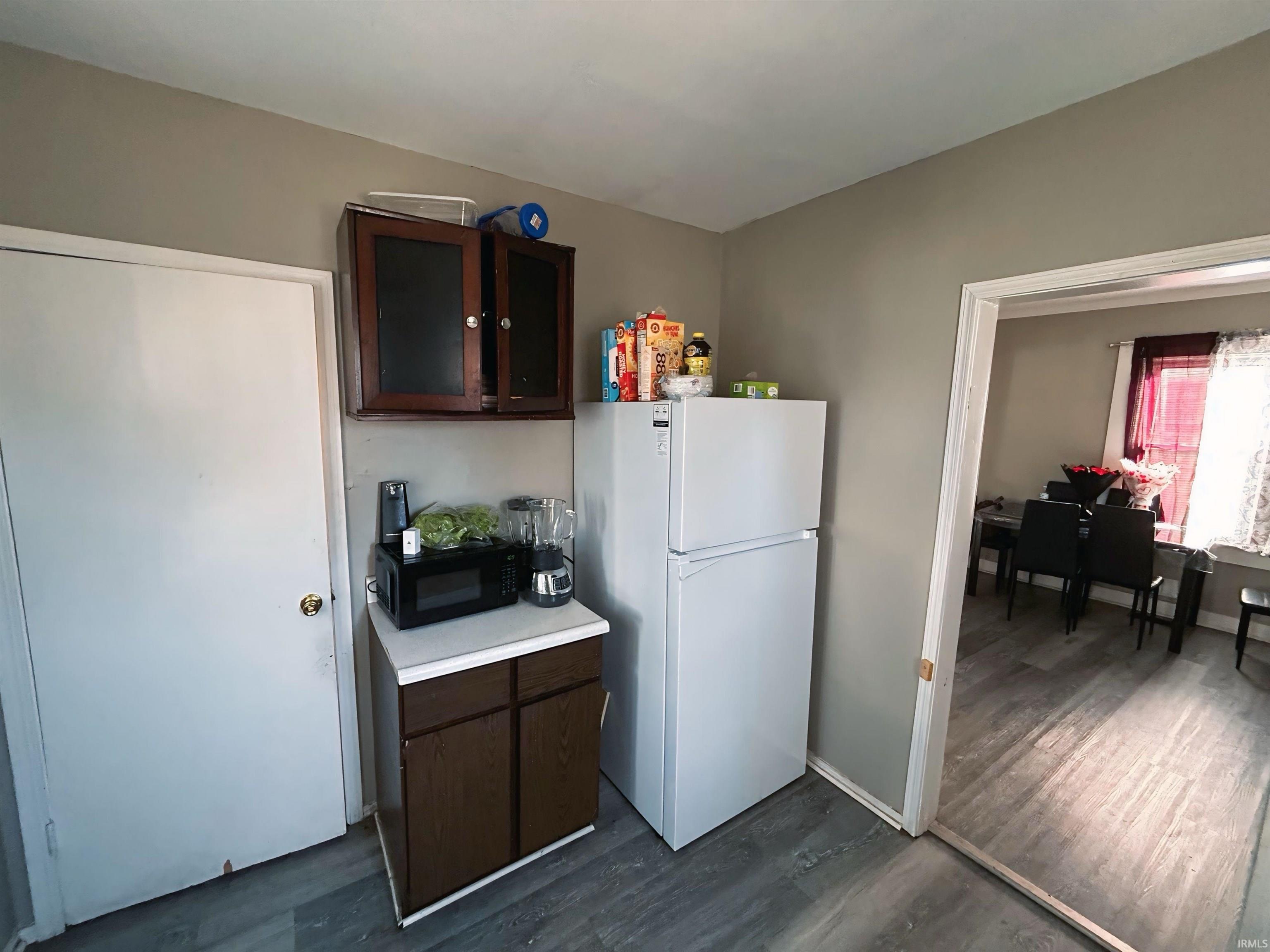 Kitchen featuring dark brown cabinets, freestanding refrigerator, dark wood-type flooring, light countertops, and black microwave