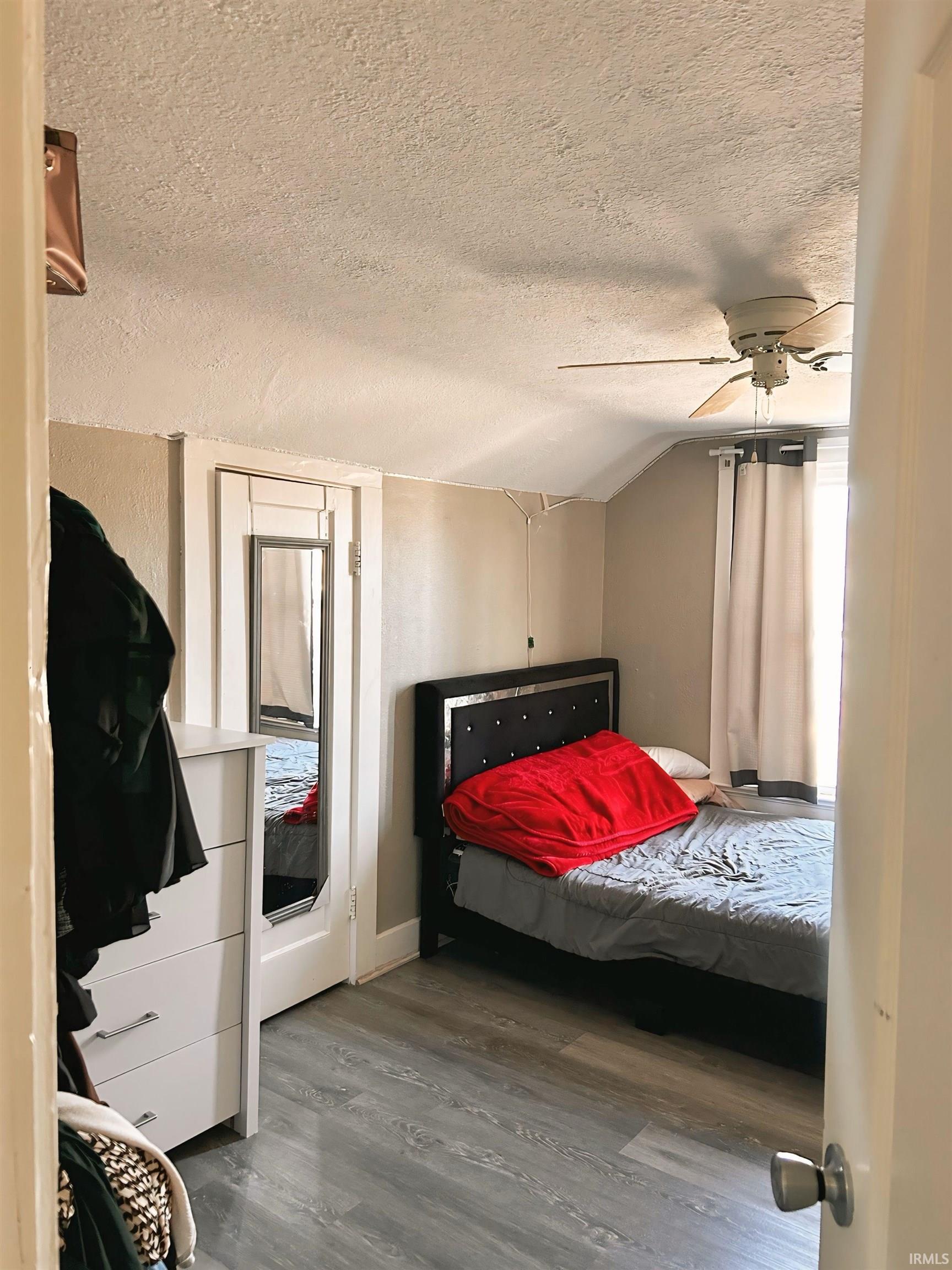 Bedroom with a textured ceiling, lofted ceiling, a ceiling fan, and wood finished floors